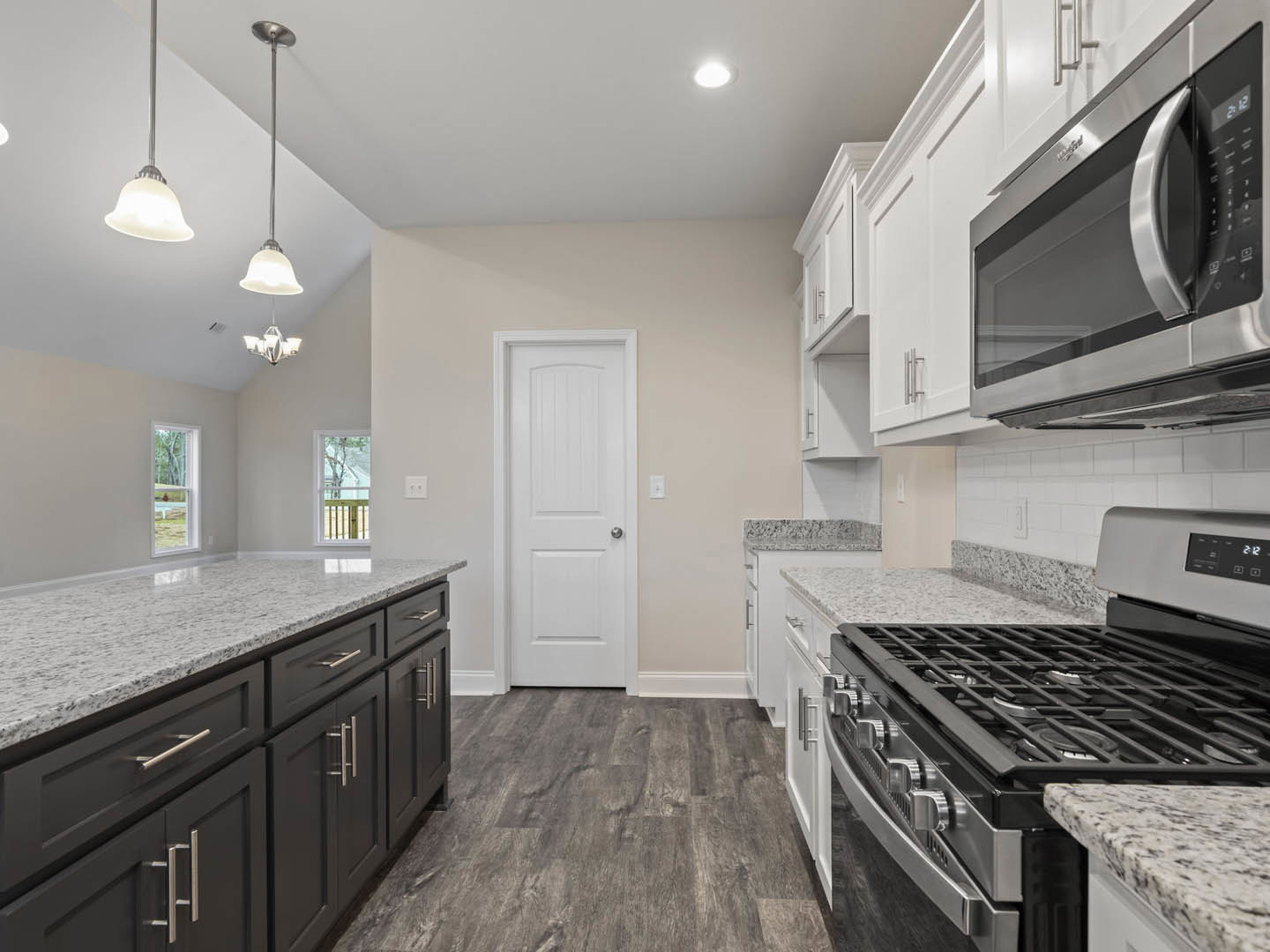 White kitchen cabinets with black stove and microwave, silver door knob on white door, clear tubular light fixture, close-up of stove and microwave, light countertops and sink.