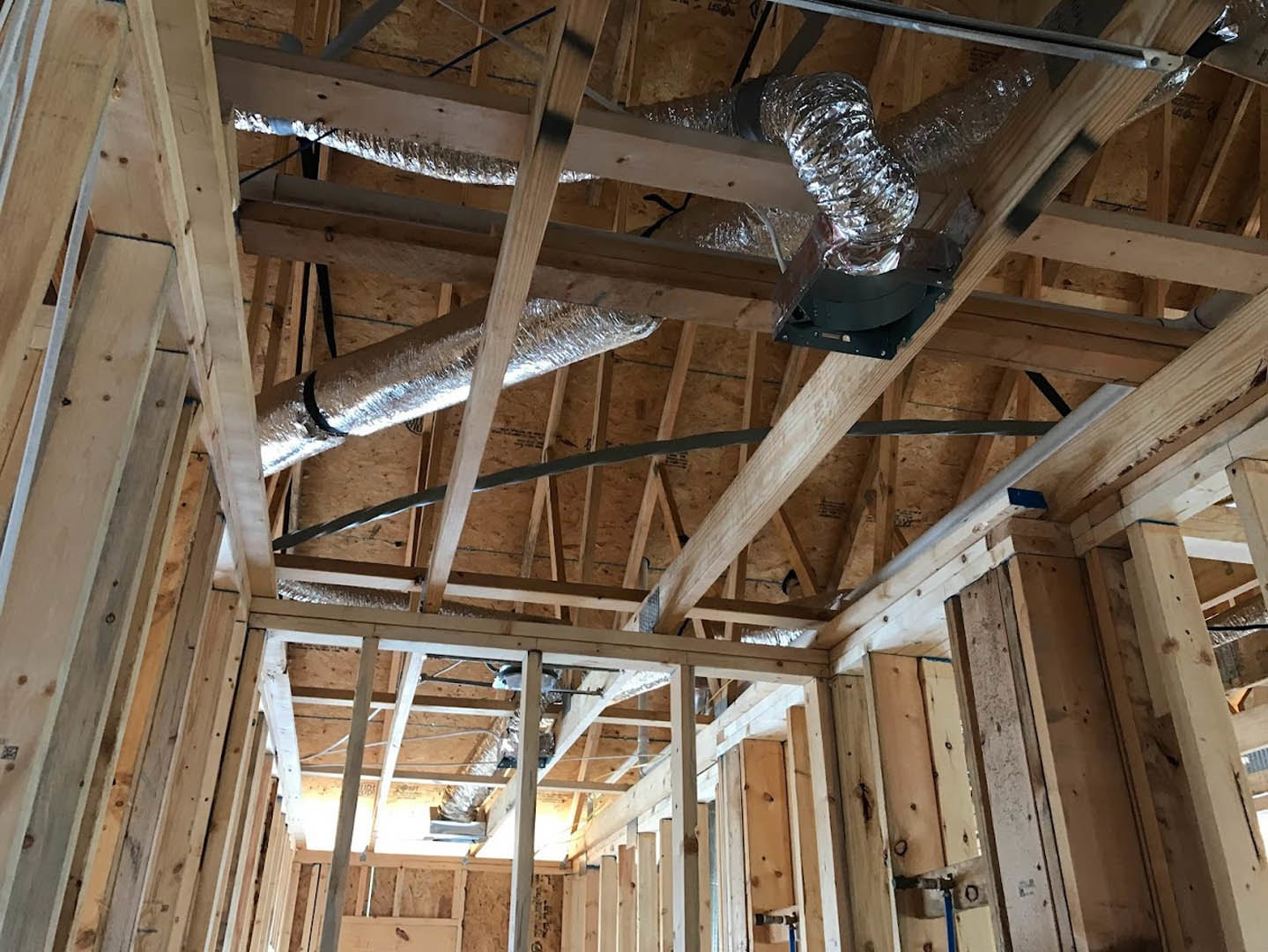 Exposed wood framing with metal vent pipe installed along unfinished ceiling, visible insulation between beams