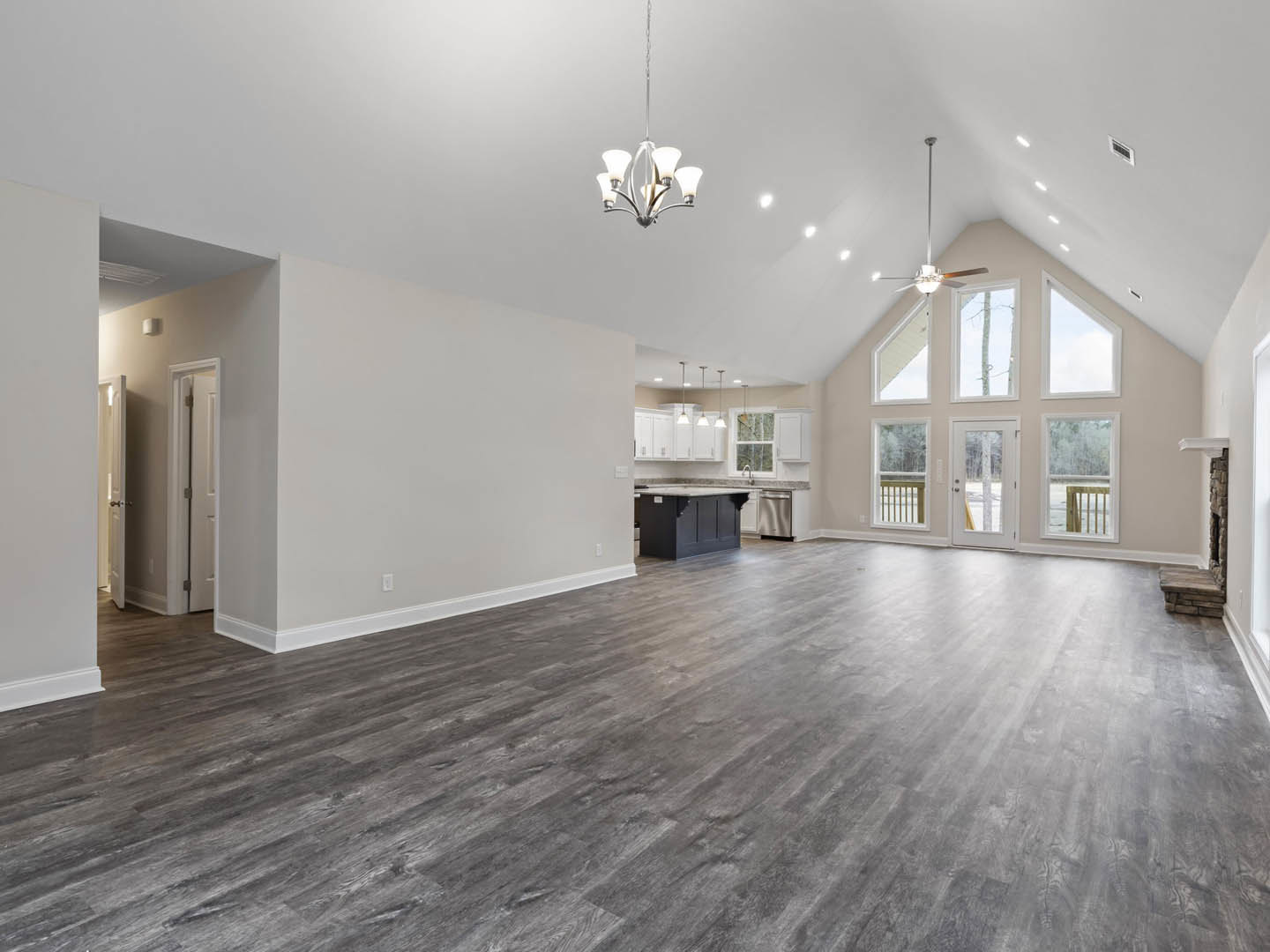 Spacious room with hardwood flooring, wood baseboards, ceiling fan with five lights, white door featuring a window, and neutral plaster walls