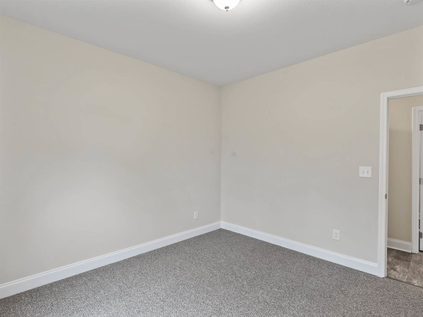 Grey carpeted floor, white walls, white ceiling with recessed light fixture, white door and door frame in a modern interior room