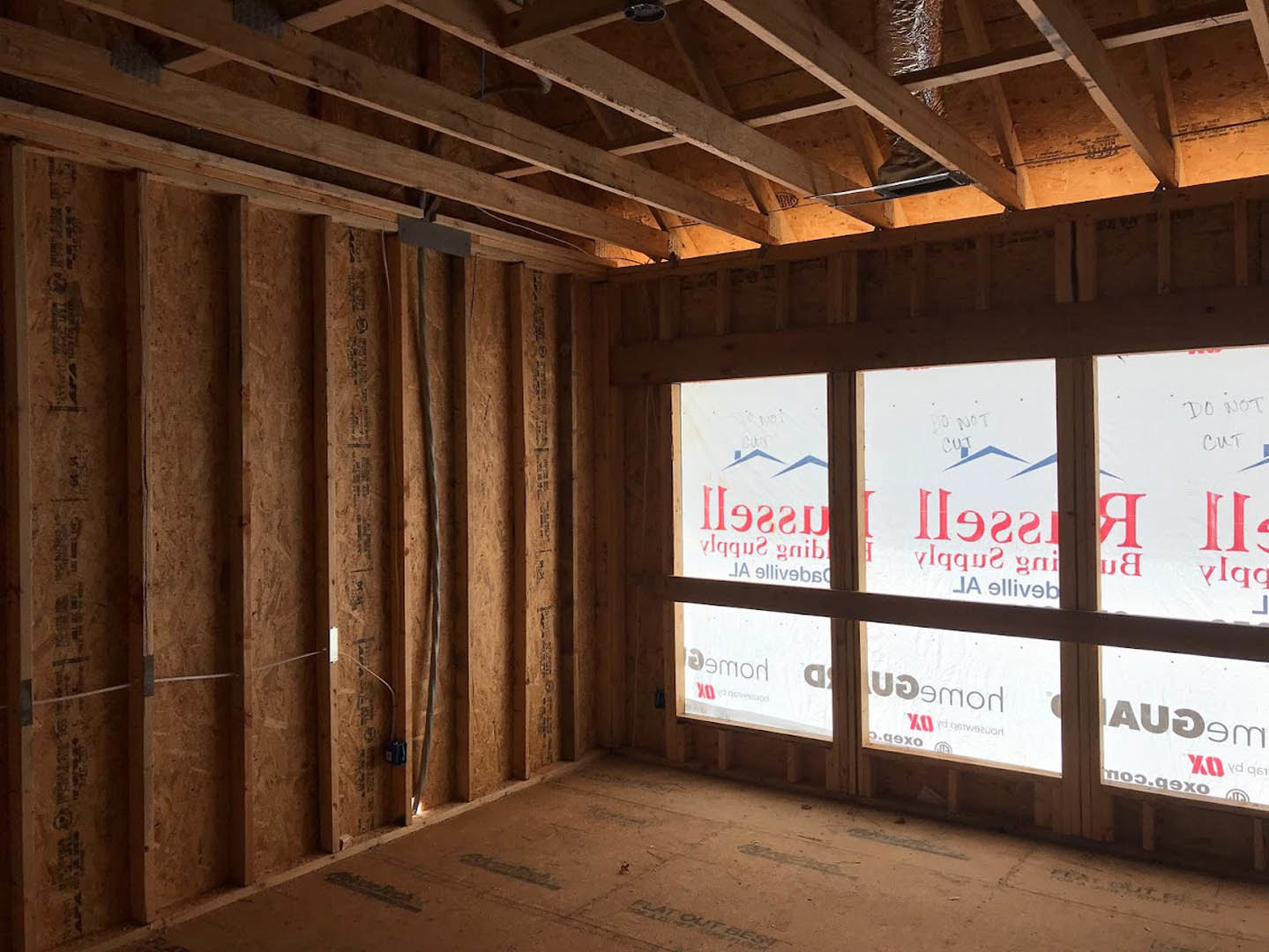 Spacious room featuring exposed wooden ceiling beams, multiple windows with white plastic coverings, unfinished flooring, and a white sign with red text leaning against a wall.