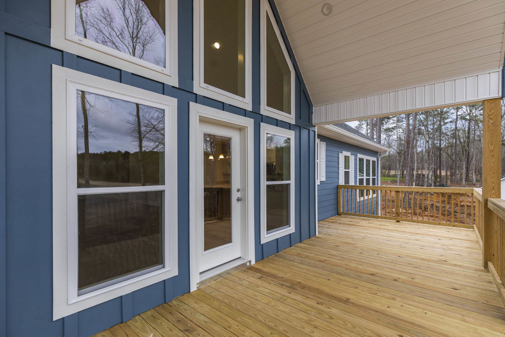 Wooden deck with glass door, porch area, close-up of wooden railing, large windows overlooking trees and fenced yard, hardwood flooring