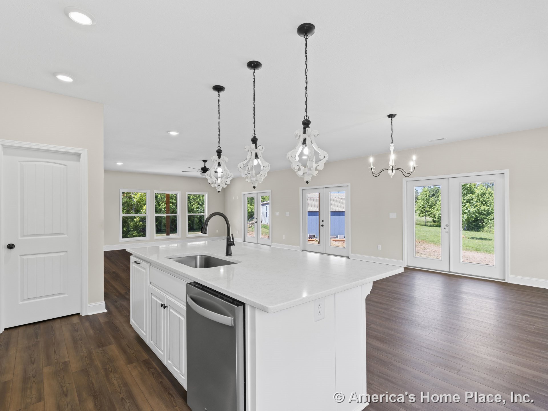 Open concept kitchen with large white island featuring quartz countertops and built-in sink, pendant lighting overhead, white cabinetry, wood-look flooring, recessed lighting, and