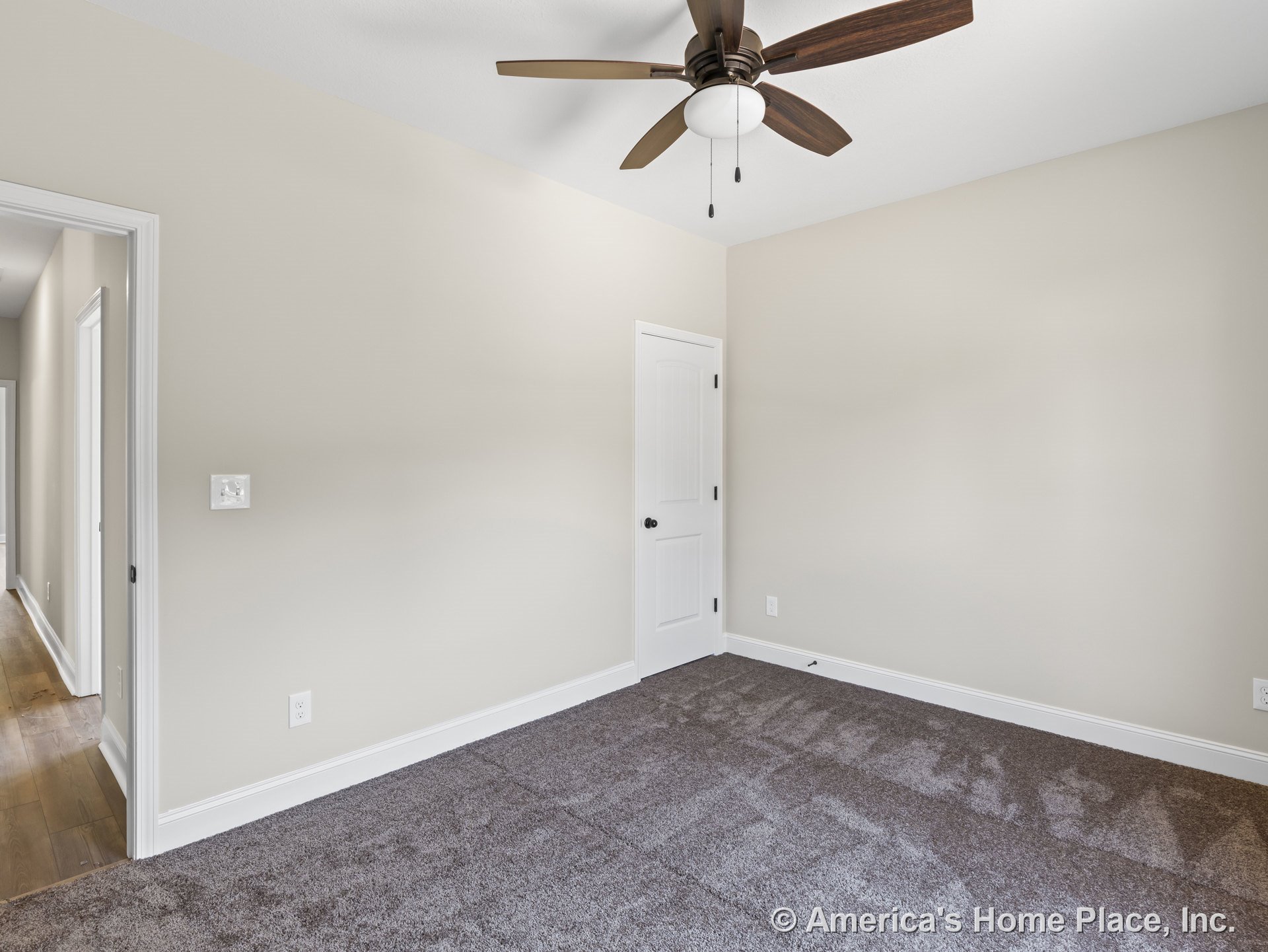 Bedroom with neutral painted walls, carpeted floor, white trim and baseboards, ceiling fan with light fixture, paneled interior door, and hallway with wood flooring visible through