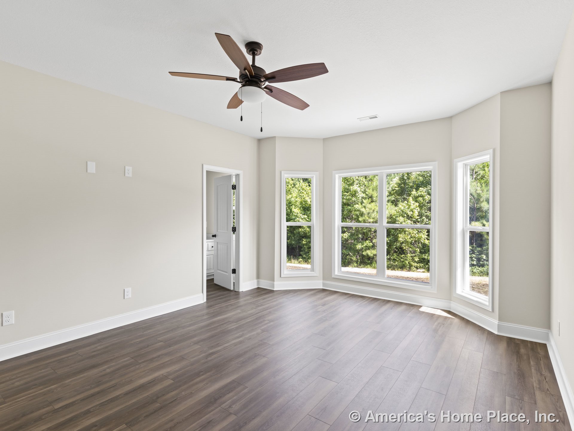 Bedroom with expansive bay windows, wood-look plank flooring, ceiling fan with light, white baseboard trim, neutral wall paint, and doorway leading to bathroom.