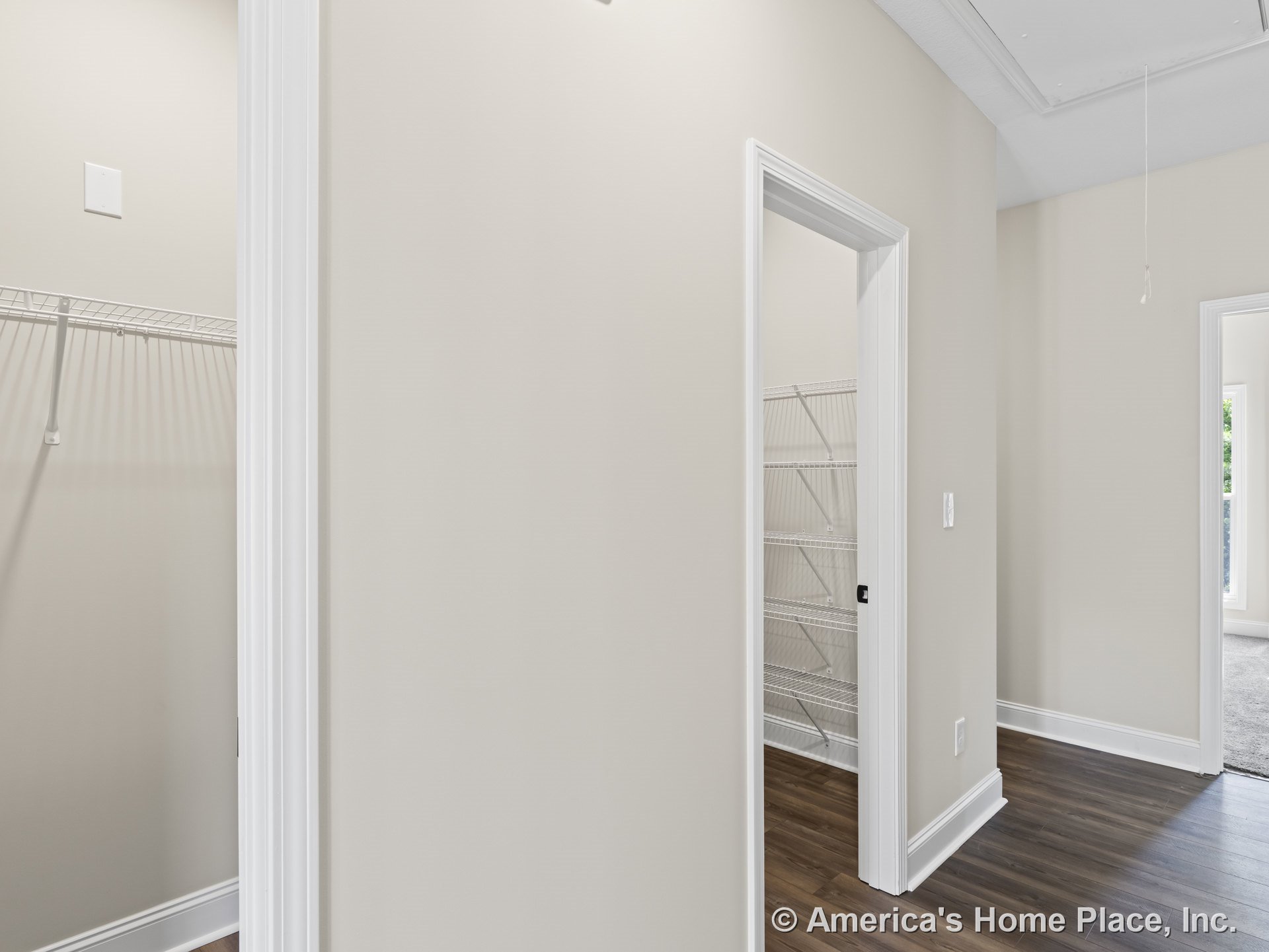Hallway with two closets featuring built-in wire shelving, wood-look flooring, white door trim, neutral wall color, baseboard molding, and attic access panel.