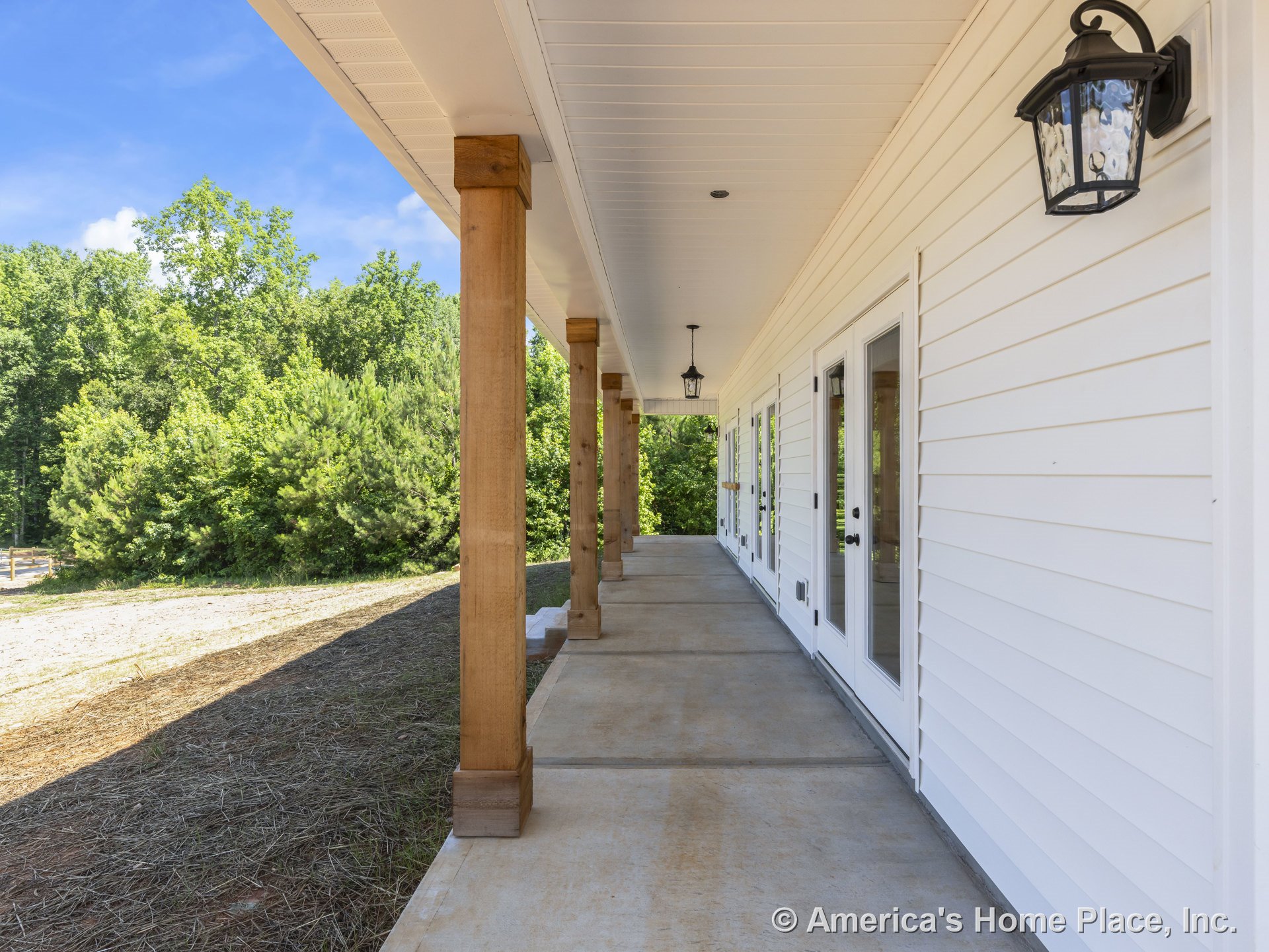 Covered porch with wood columns, concrete flooring, white horizontal siding, glass exterior doors, black lantern wall lights, and a beaded ceiling.