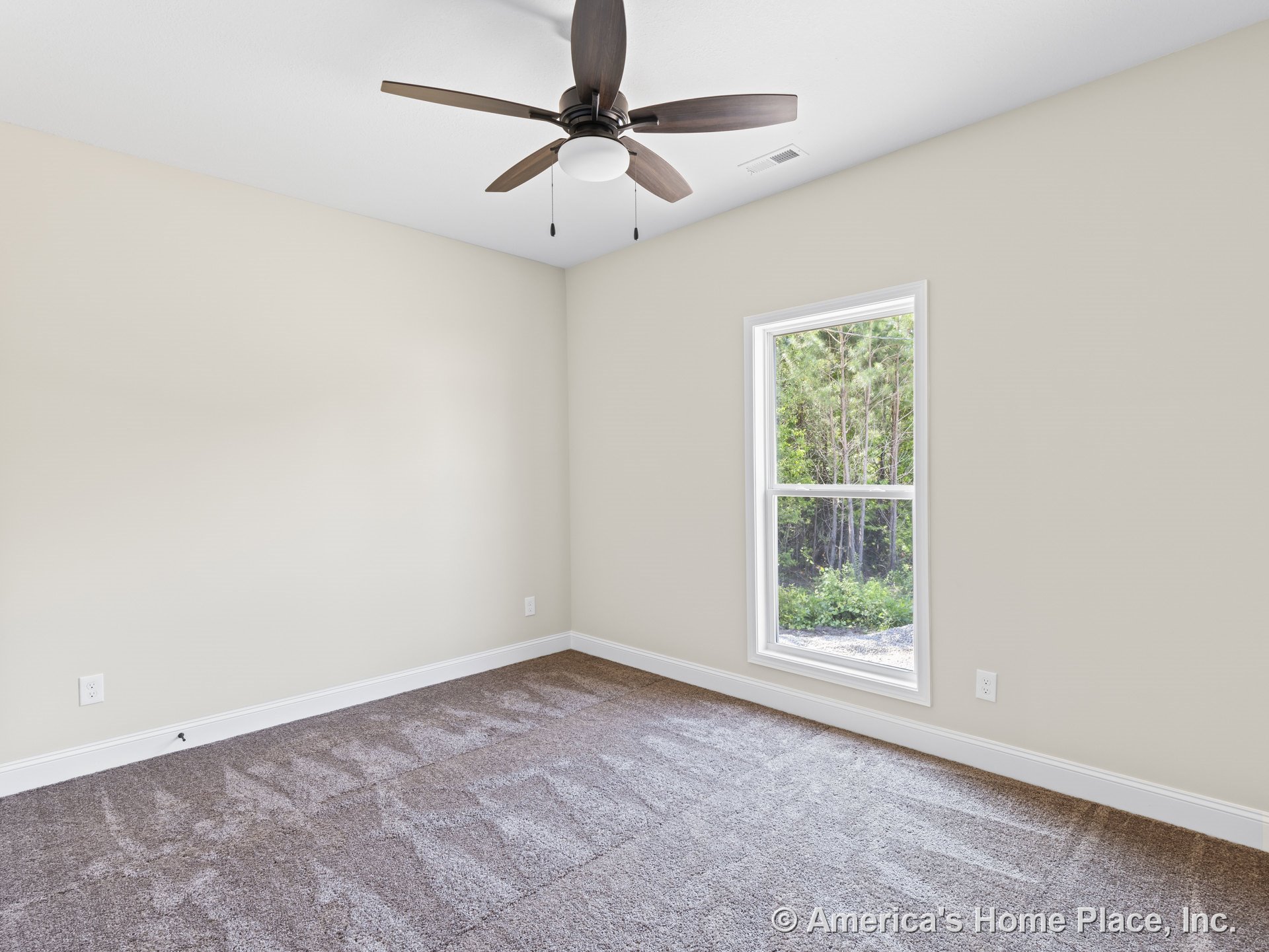 Bedroom with beige walls, brown carpet flooring, large window with white trim, ceiling fan and light fixture, white baseboards, and single electrical outlet.