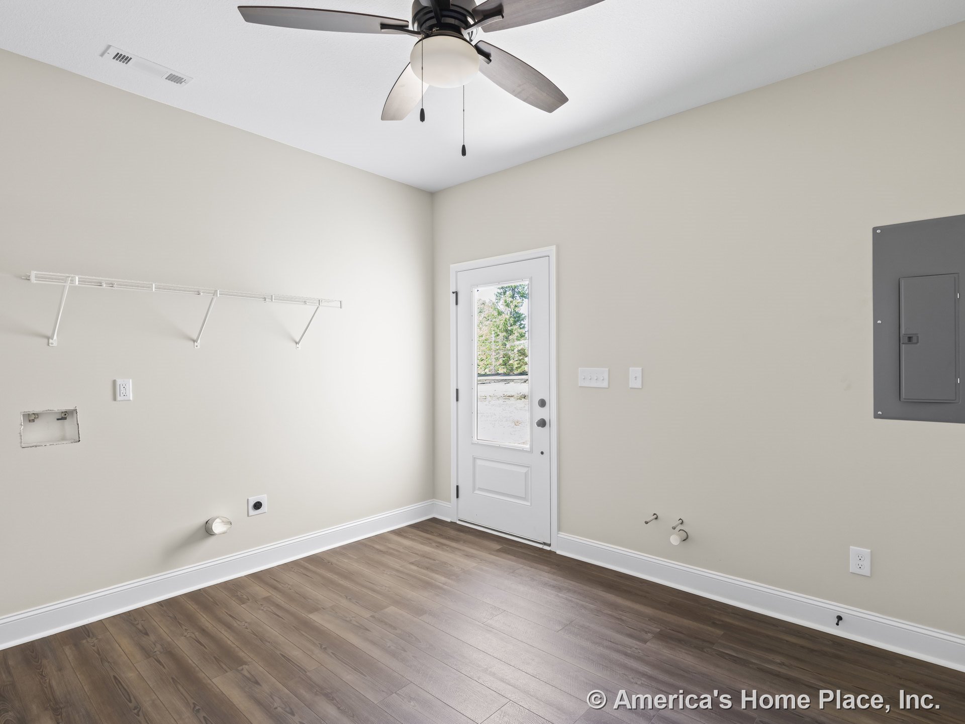Laundry room with ceiling fan and light, utility hookups on wall, white wire shelving, exterior door with window, wood-look flooring, electrical panel, baseboards, and neutral wall