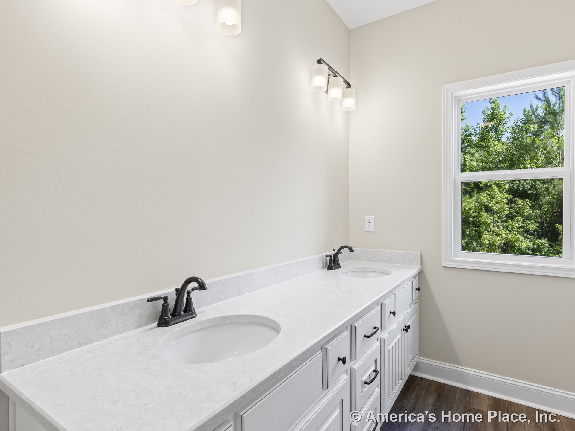 Double vanity with white cabinetry and quartz countertop, two undermount sinks with matte black faucets, three-light wall fixture above, large window with trim, neutral wall color