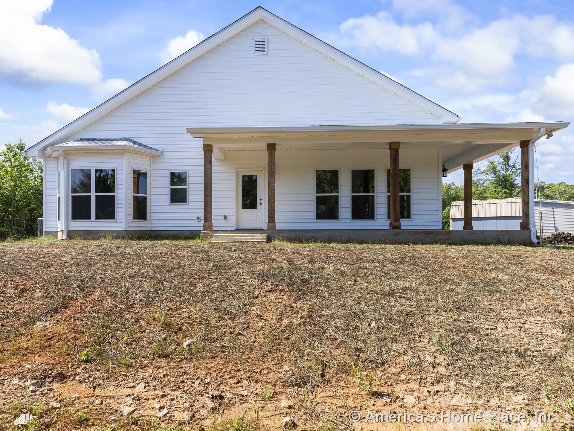 Large covered front porch with wood support columns, white siding exterior, multiple large windows including a bay window, gable roof, front entry door, and permanent lighting
