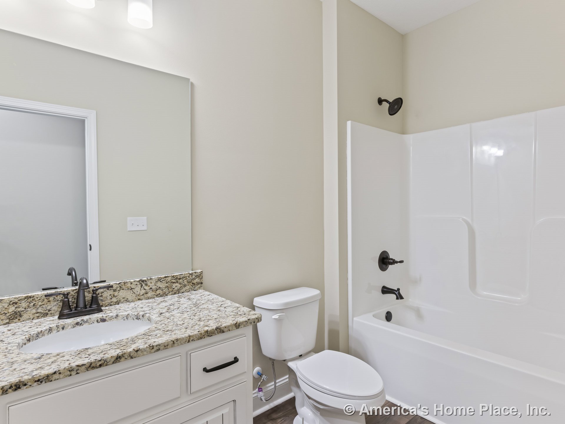 Granite countertop vanity with white shaker cabinets, built-in bathtub and shower, wall-mounted lighting above mirror, dark bronze plumbing fixtures, wood-look flooring, neutral