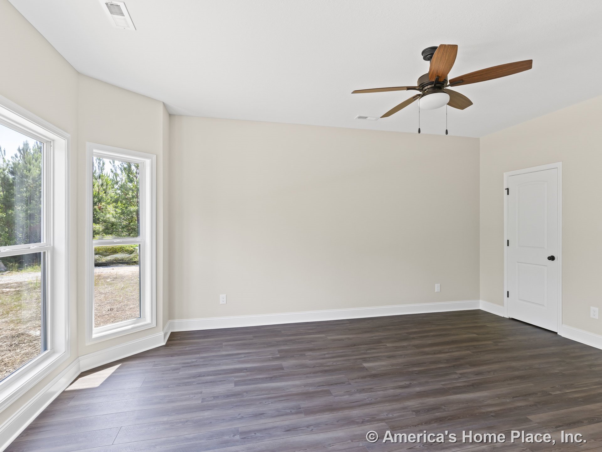 Spacious bedroom with large bay windows, wood-look flooring, ceiling fan with light, white trim and baseboards, neutral painted walls, and a paneled interior door.