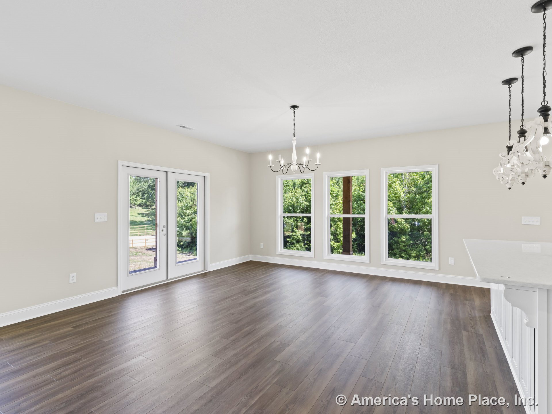 Tall windows and double glass doors fill the open living area with natural light, highlighting wood-look plank flooring, white baseboard trim, neutral walls, and a modern