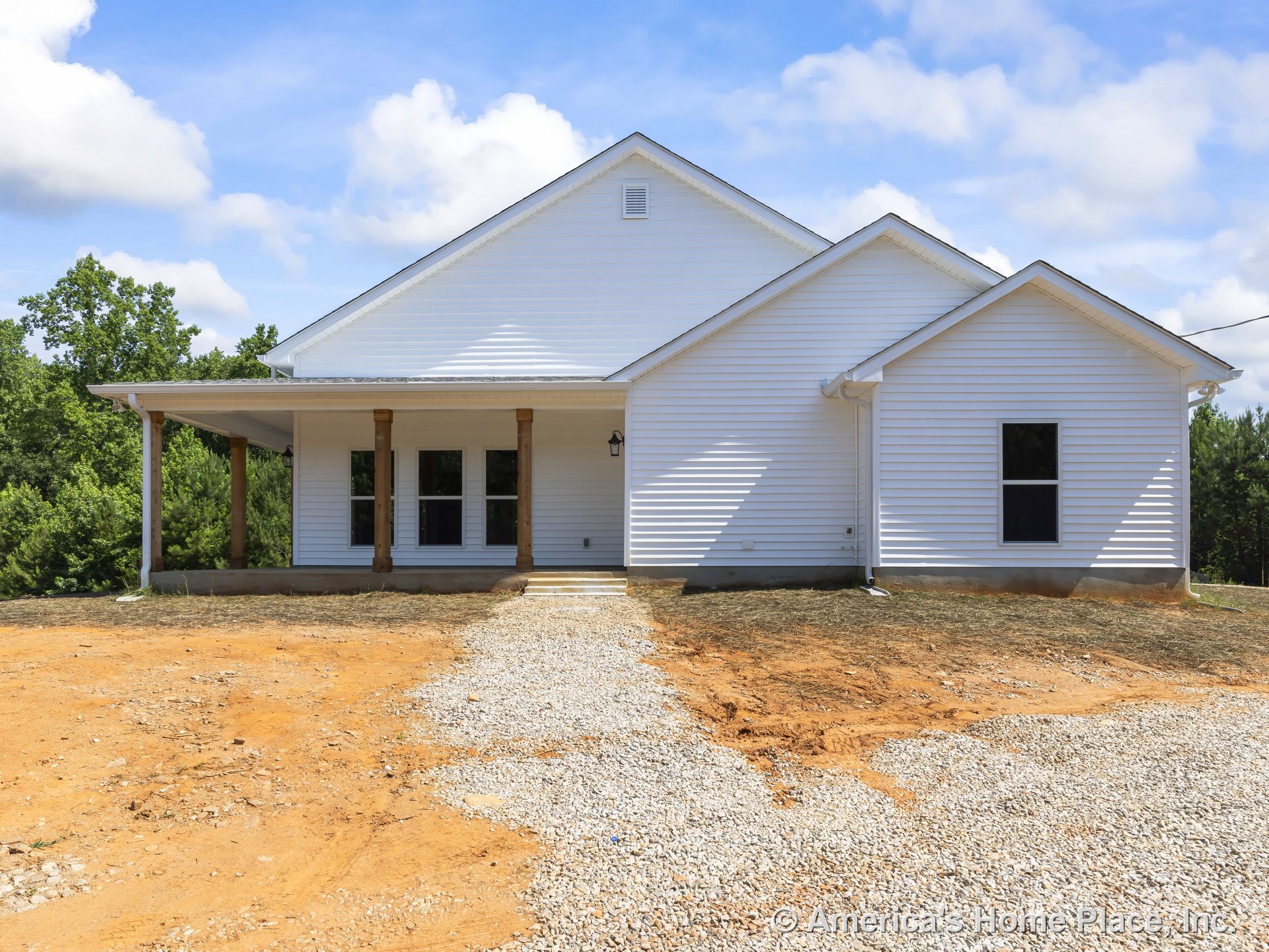 White horizontal siding and gable roof with permanent lighting, covered front porch supported by wooden columns, multiple double-hung windows, gravel driveway, rural setting.