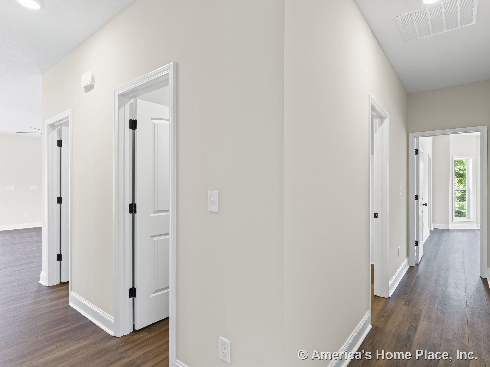Hallway with multiple white paneled doors, wood-look plank flooring, beige painted walls, white baseboards and trim, recessed ceiling lighting, large window at hallway end, and