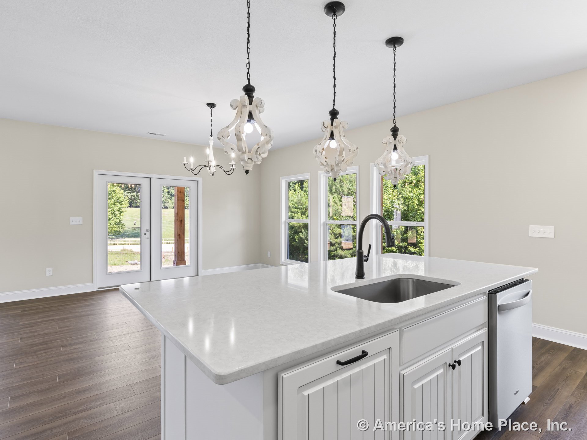 Large kitchen island with white shaker cabinets and quartz countertops, three pendant lights overhead, stainless steel dishwasher, double French doors, wood plank flooring, open