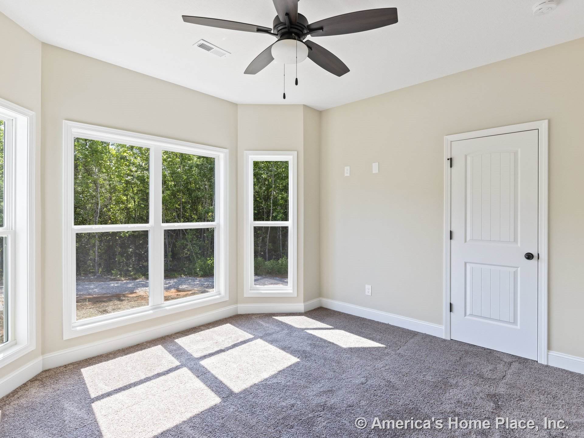 Bedroom with large corner windows framed in white trim, beige walls, carpet flooring, ceiling fan with built-in lighting, paneled door, and modern baseboards.