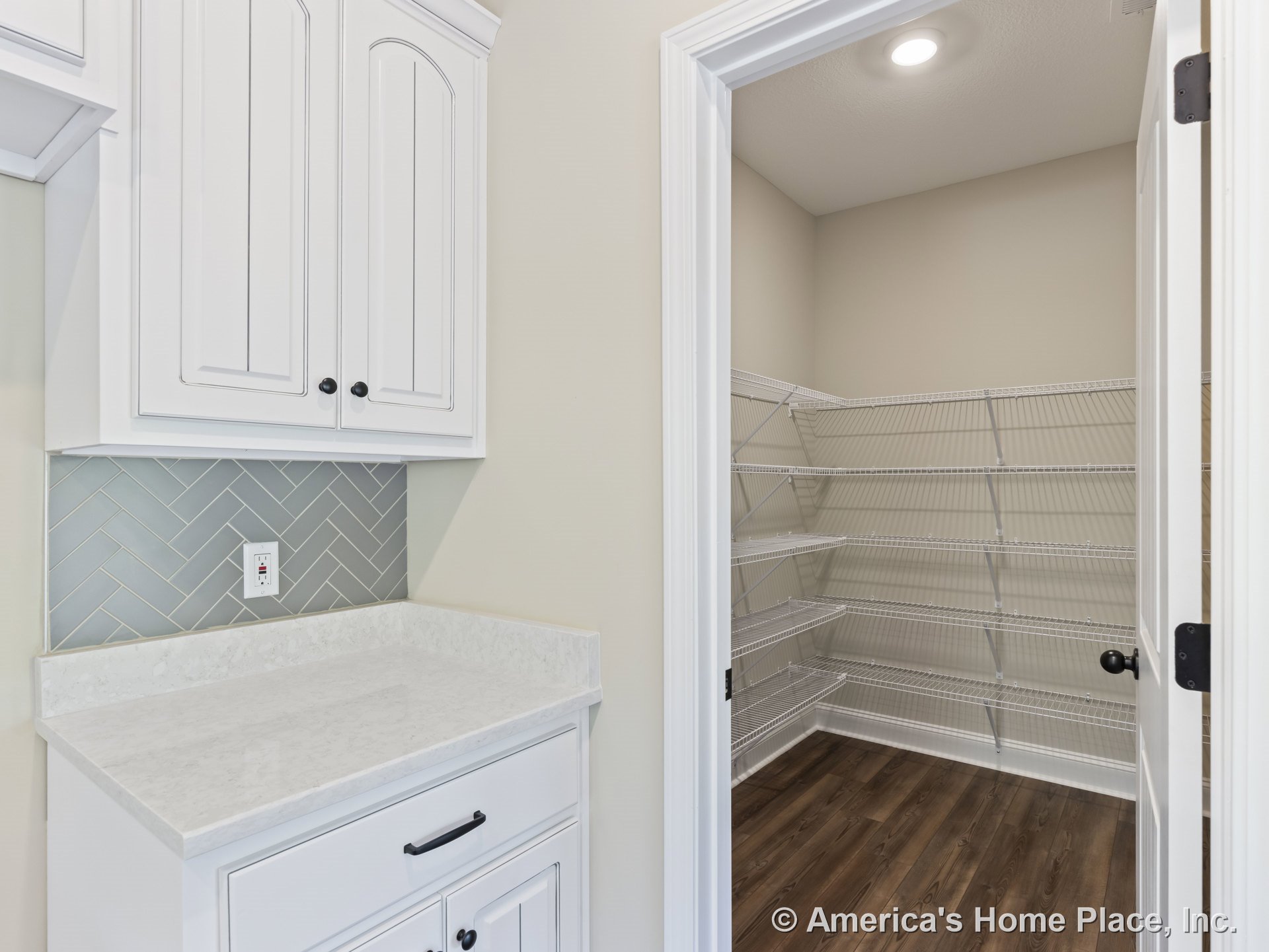 Walk-in pantry with wire shelving next to kitchen area featuring white upper cabinets, herringbone tile backsplash, quartz countertop, recessed ceiling light, and wood-look