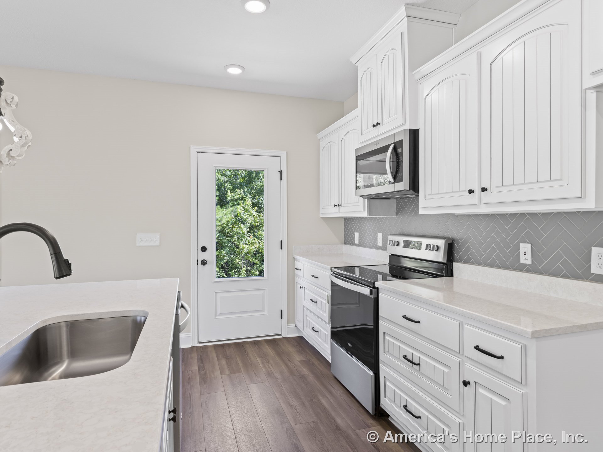White shaker cabinets with quartz countertops, herringbone tile backsplash, stainless steel appliances, wood-look flooring, glass exterior door, and recessed lighting