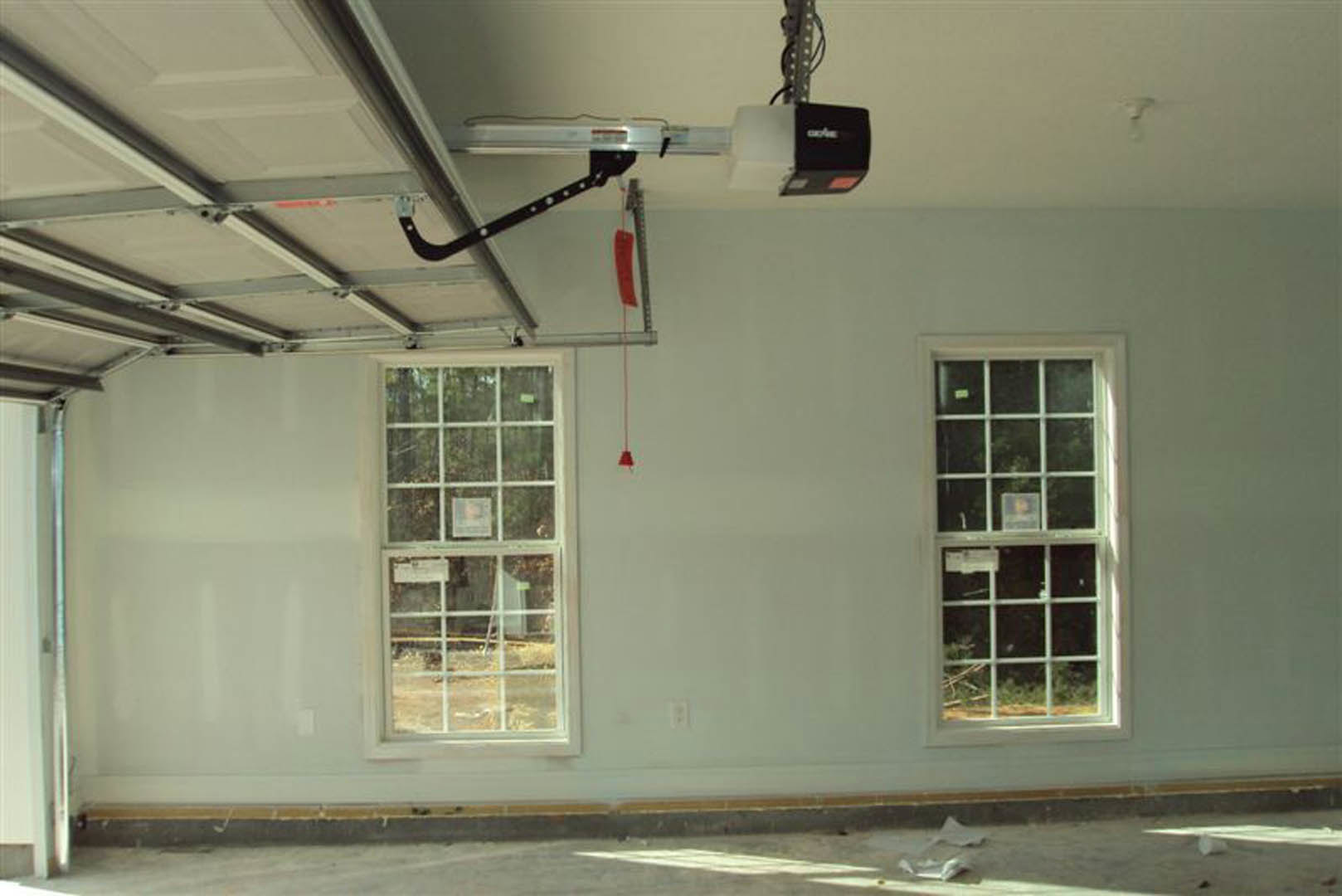 Garage door installed along a plaster wall in a residential room with daylight streaming through a window, visible ceiling fixtures, and smooth indoor finishes.