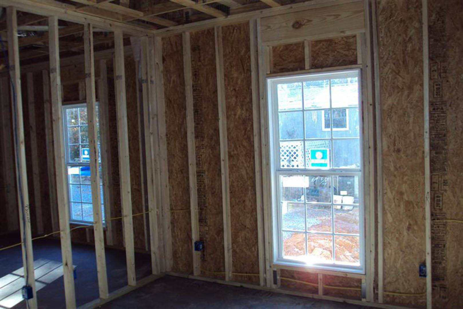 Room featuring multiple windows with wooden frames, visible insulation, and exposed wood beams, with a wooden box placed near the window.