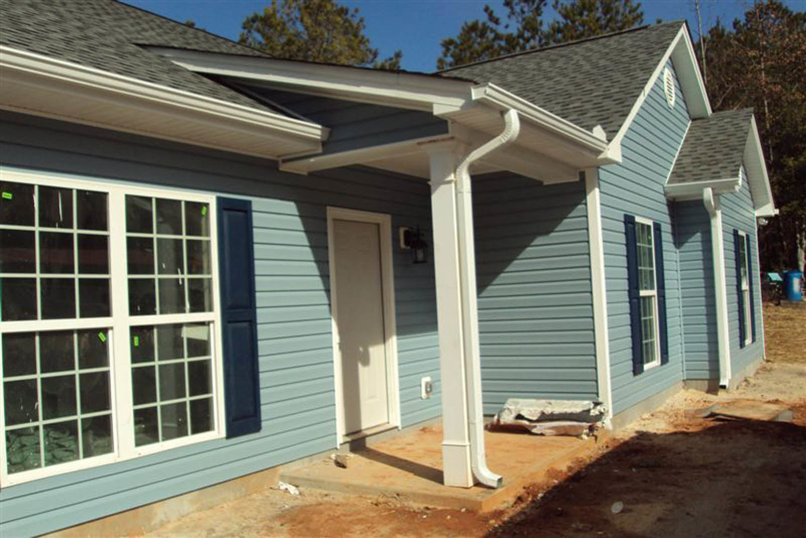 Partially built house with white column on porch, white roof, multiple windows, and light-colored siding under clear sky