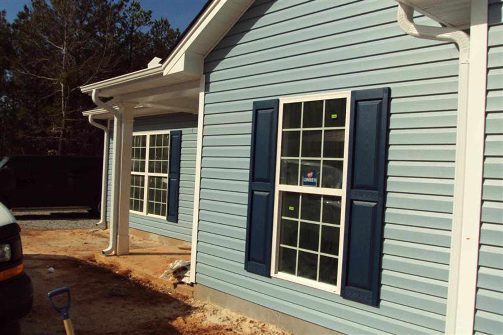 Blue siding exterior with white-trimmed window displaying a sign, blurred face visible behind glass, black rectangular object on dark background, close-up of metal shovel, and