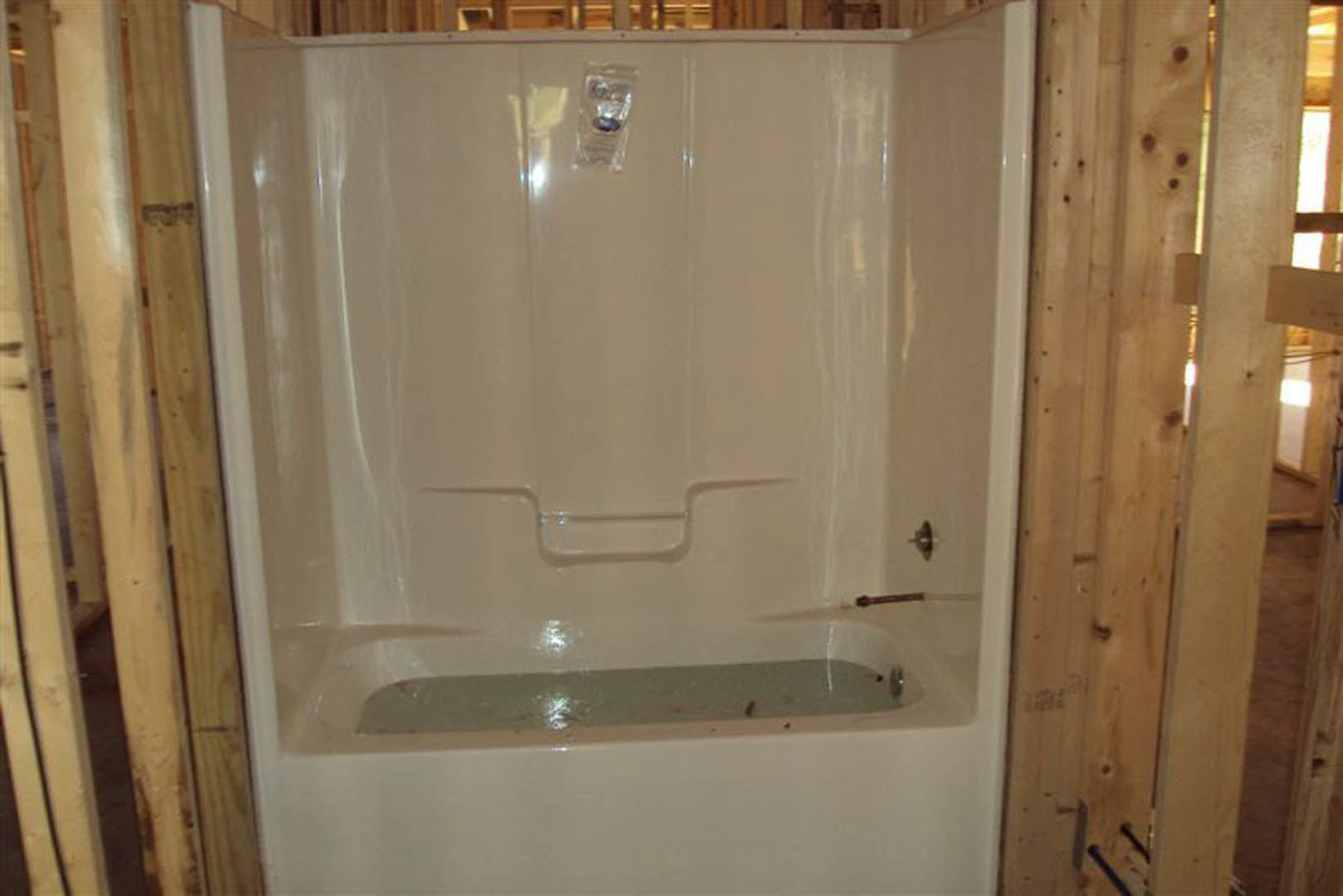 Freestanding white bathtub on light wood floor with wood-paneled walls in a modern bathroom
