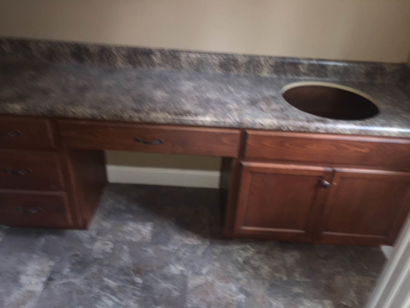 Granite kitchen countertop with round sink, white cabinetry, and drawers visible in background