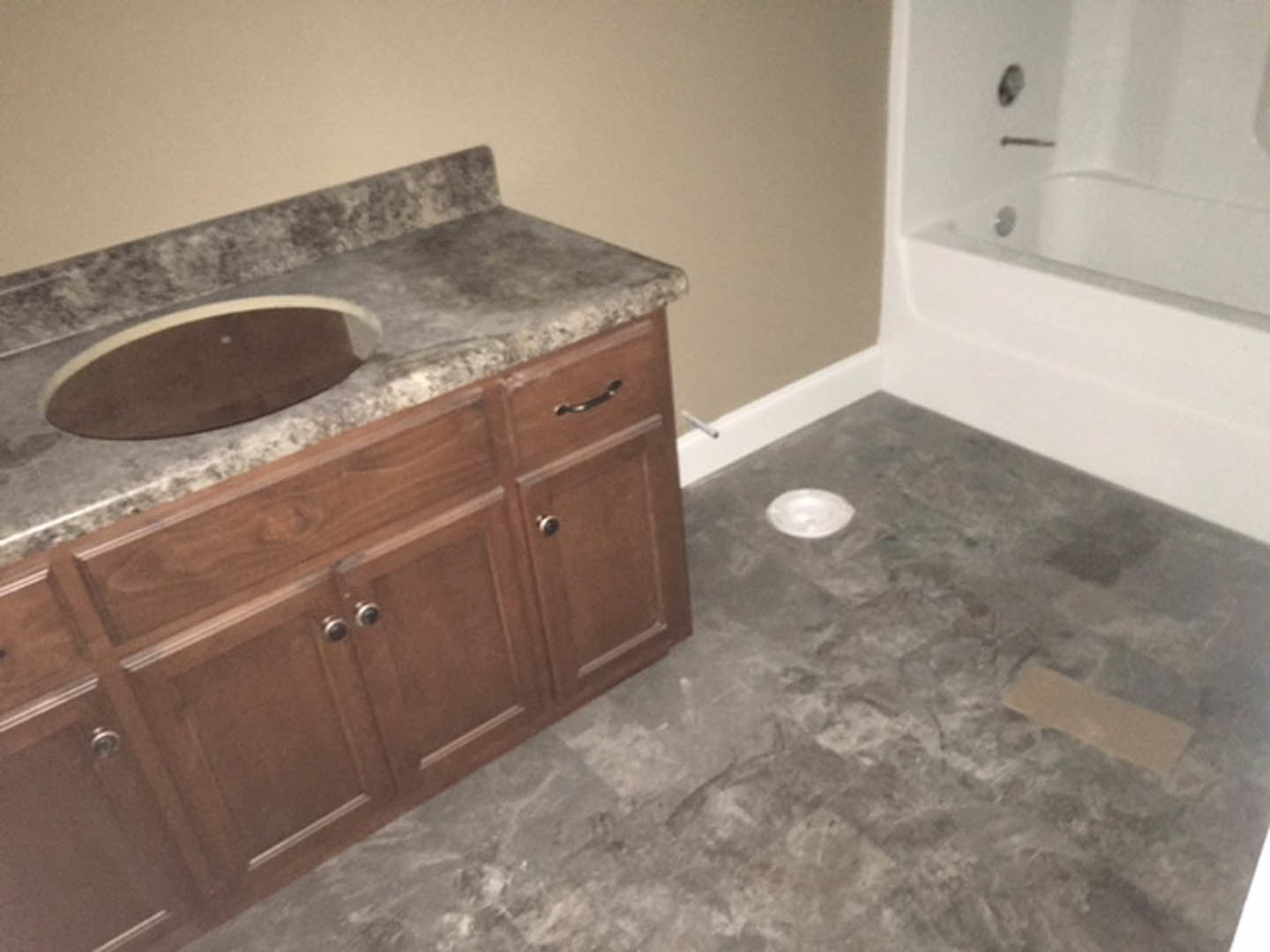 Modern bathroom featuring a granite countertop with an undermount sink, chrome faucet, freestanding white bathtub, light gray tile flooring, and wood cabinetry with drawers.