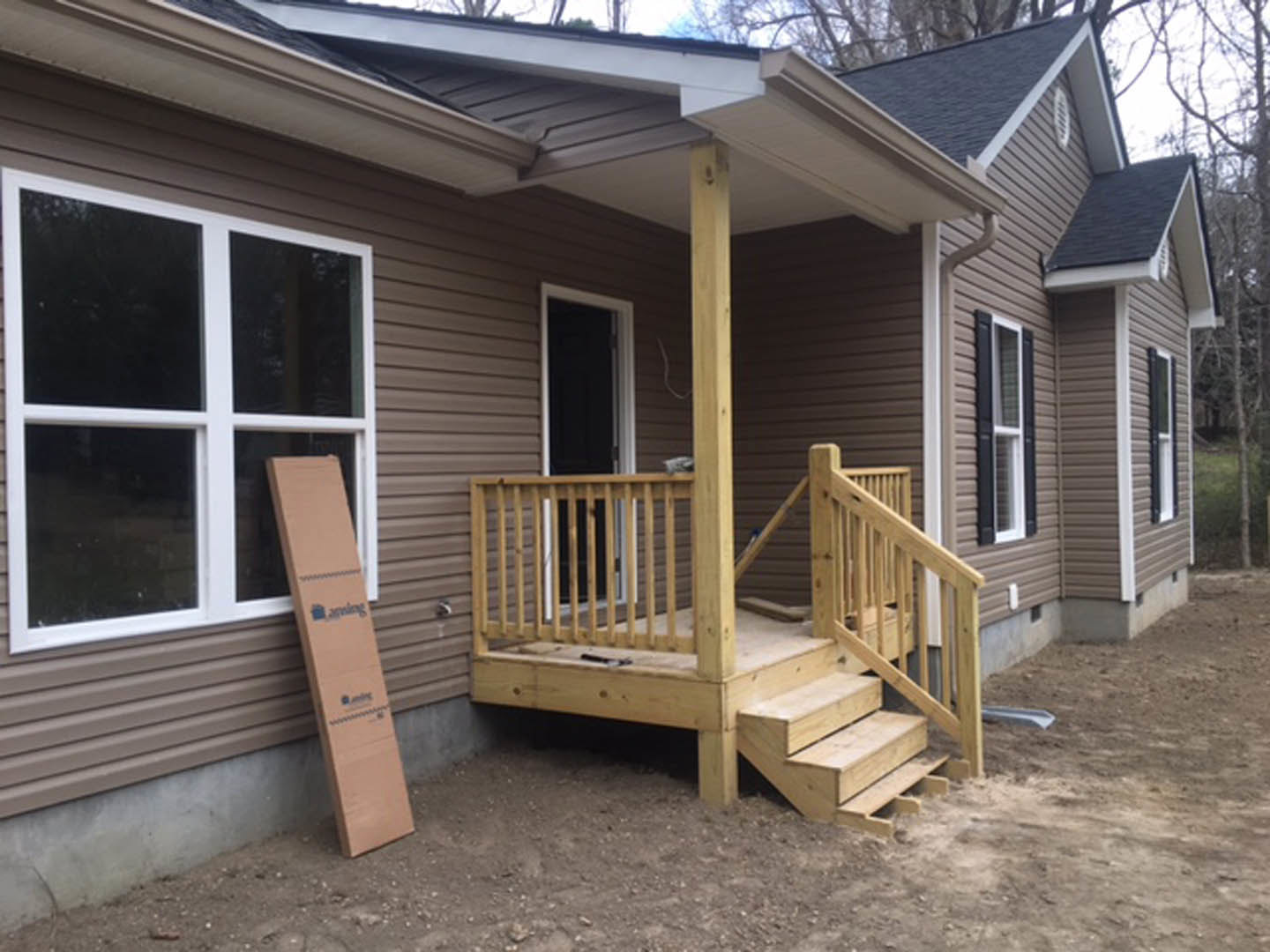 Wooden porch with stairs leading to a white-framed window, cardboard box leaning against siding, horizontal wood siding exterior
