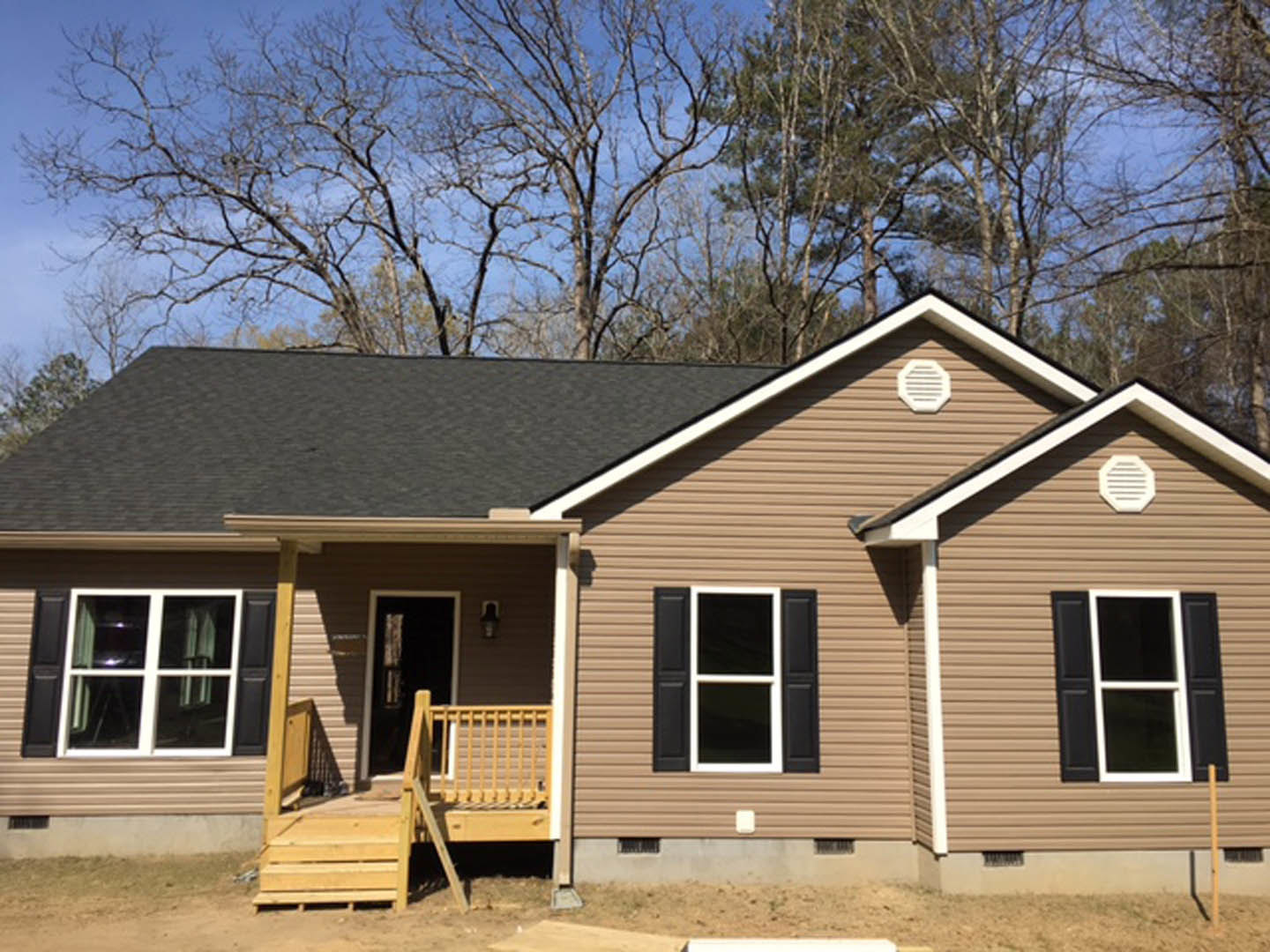Two-story cottage with wood siding, covered front porch, black door, white vent, leafless trees, and wooden fence.