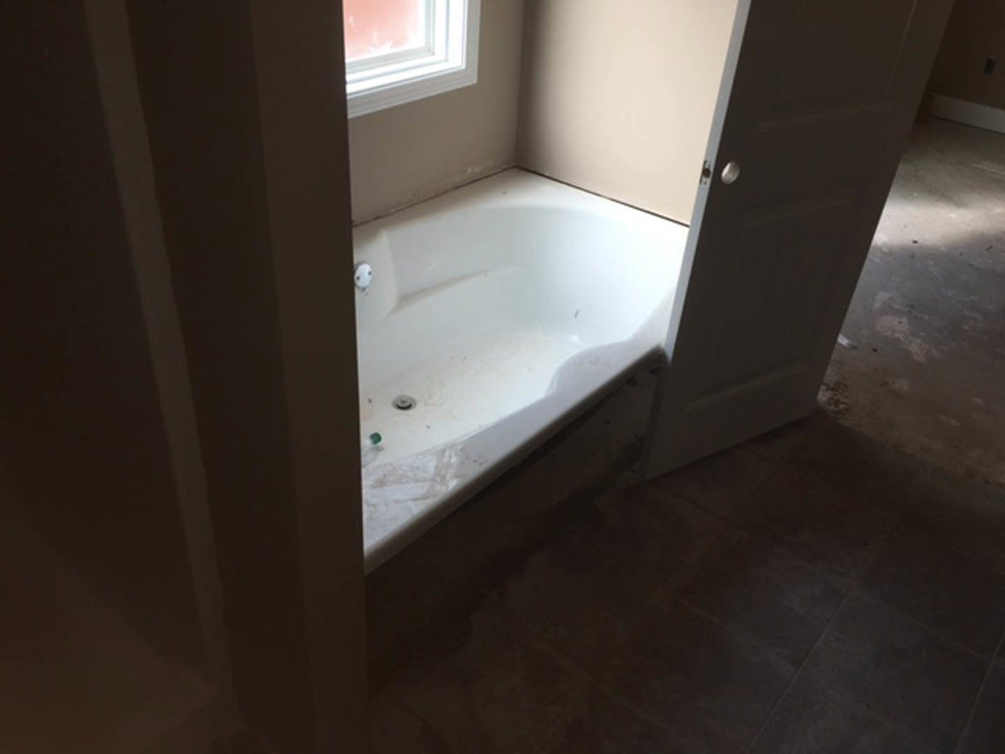 Freestanding white bathtub on light tile floor, surrounded by neutral walls and modern plumbing fixtures in a spacious bathroom