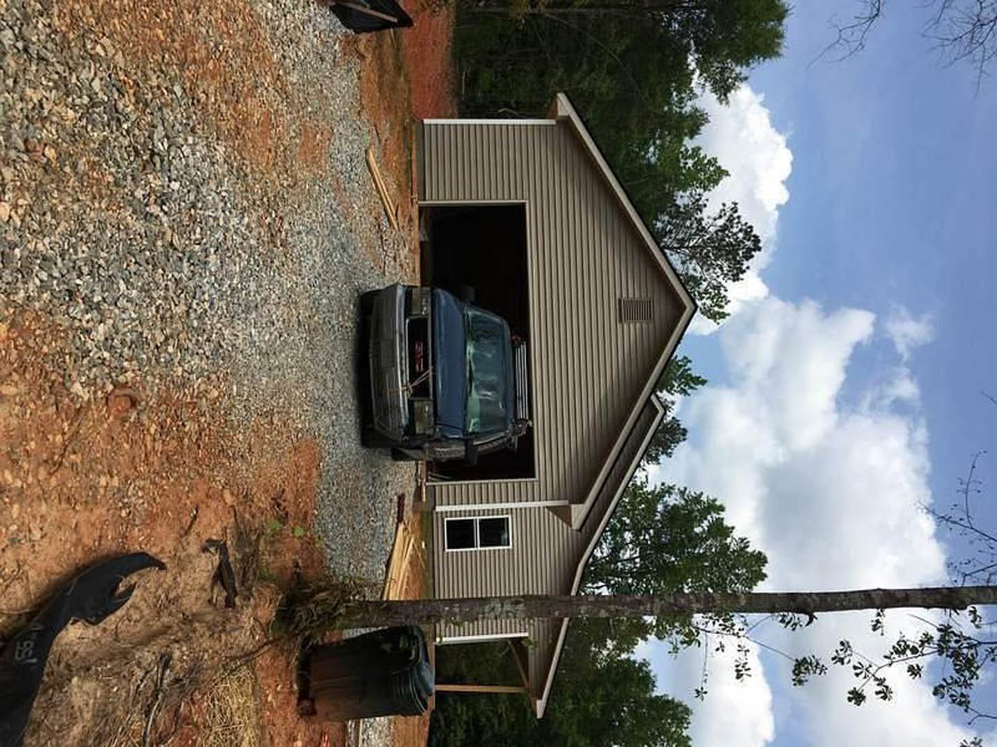 White sedan parked inside attached garage with closed door, concrete driveway, brick exterior, and windows visible on single-story home.