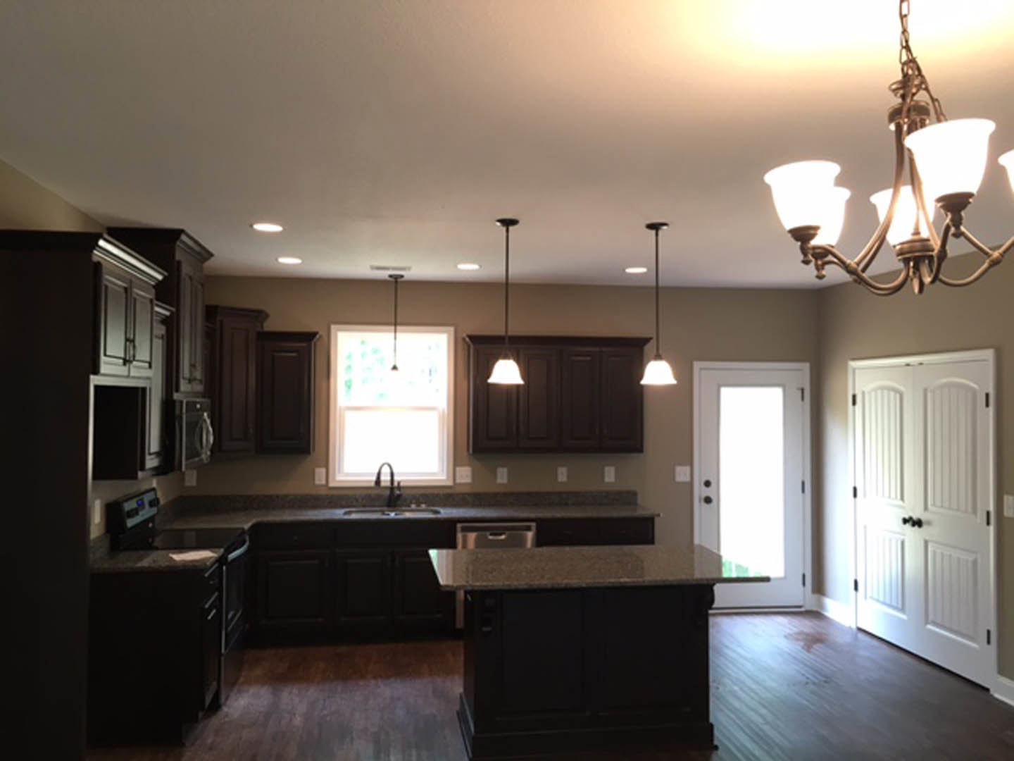Kitchen with dark wood cabinets, marble countertops, modern chandelier, stainless steel sink, and white door illuminated by natural light from nearby window