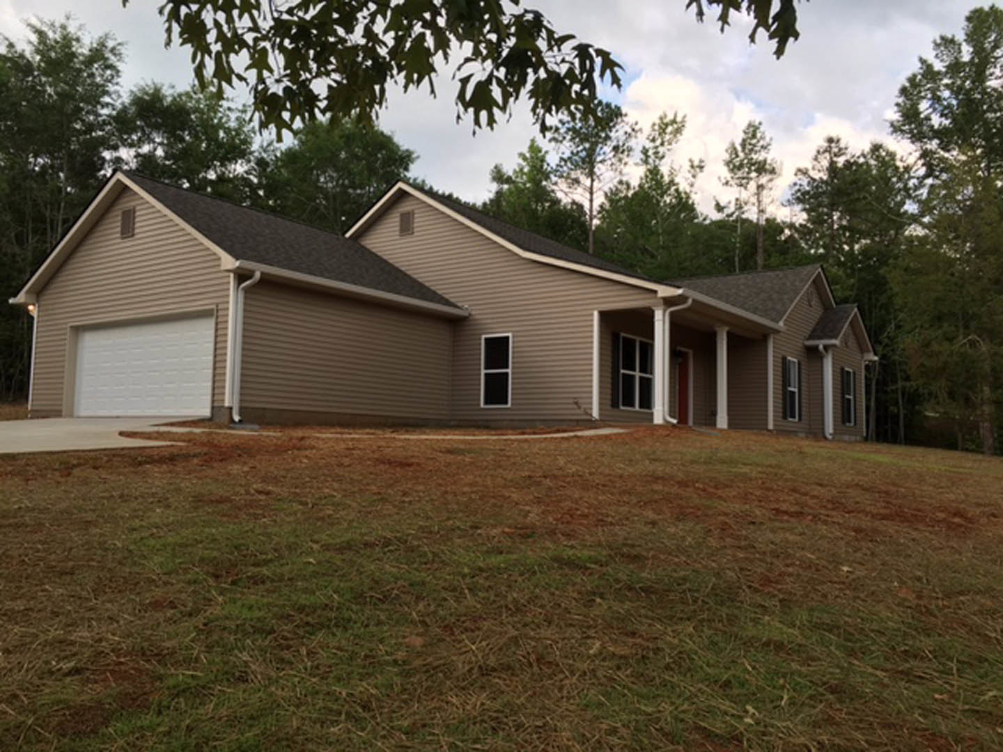 White siding house with attached garage, grassy lawn, large windows, and leafy tree branches in foreground