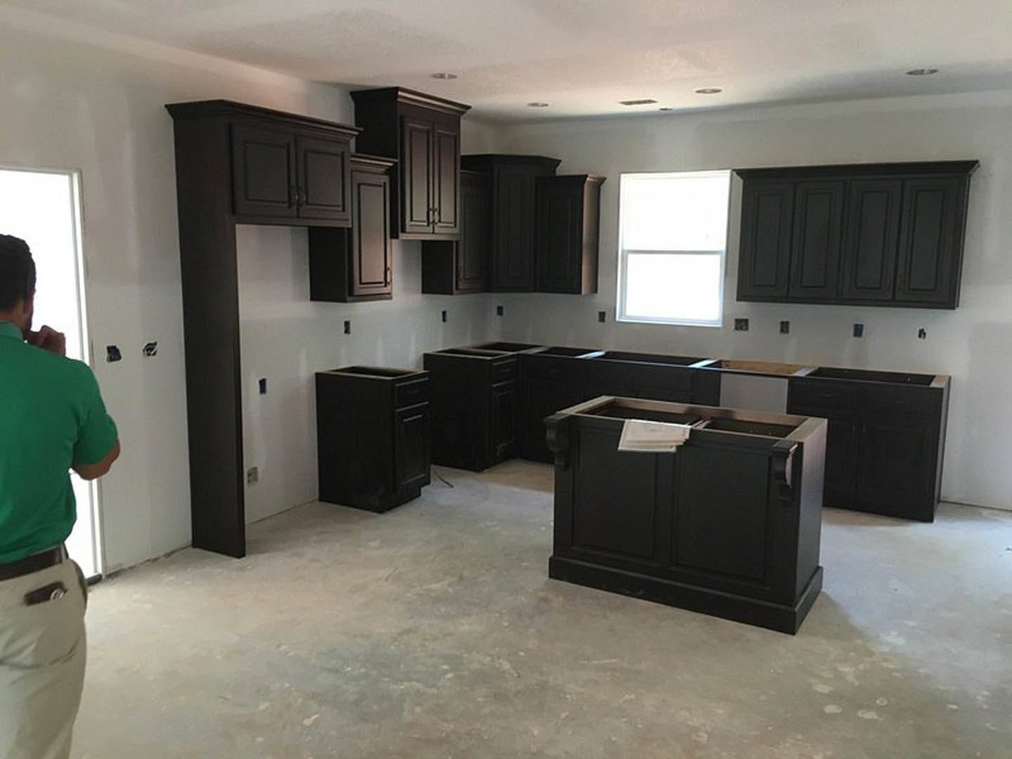 Kitchen featuring dark wood cabinets, black drawer fronts, stone countertops, large window, and a person in a green shirt standing near a black wooden trash can.