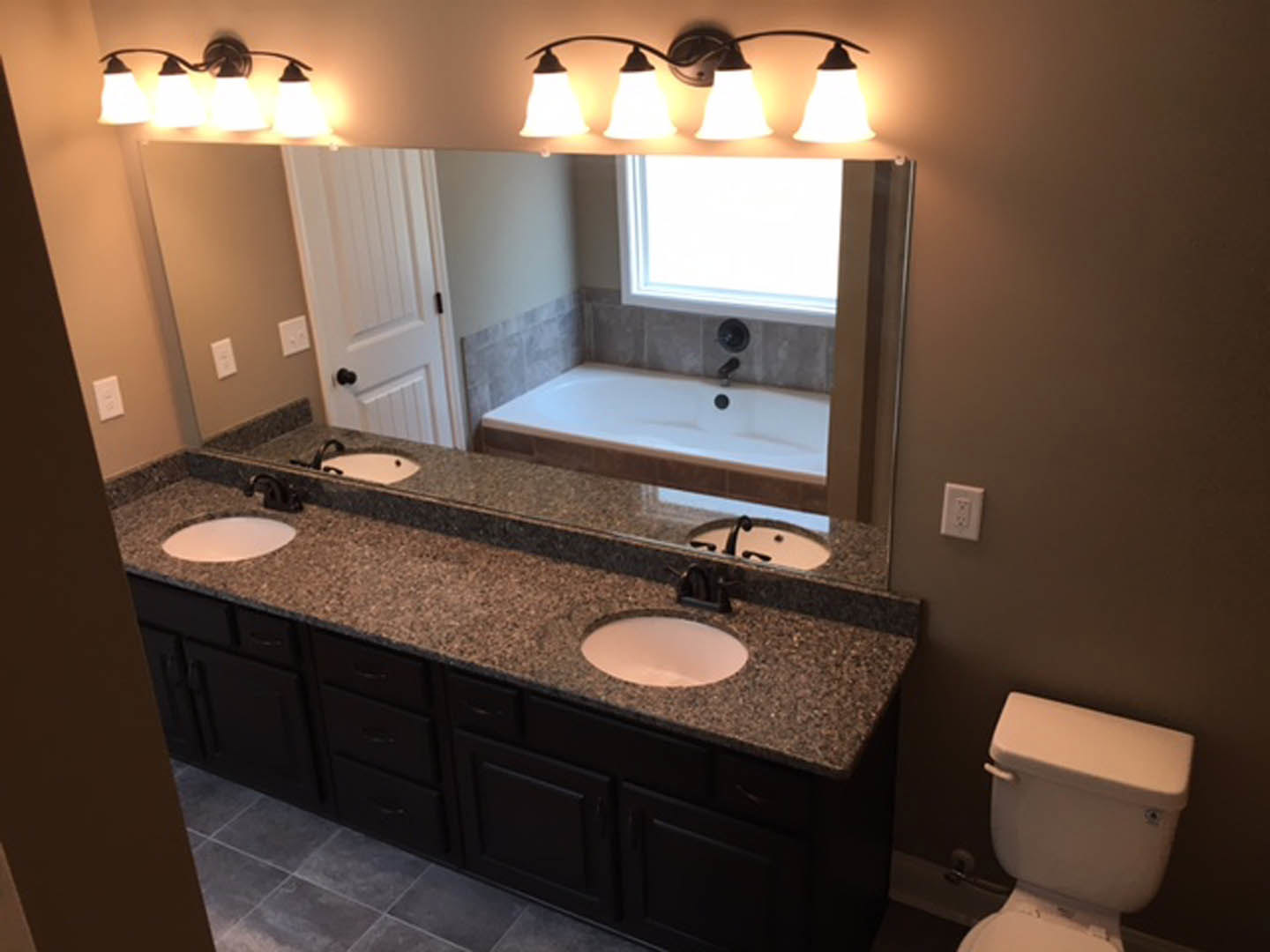 Bathroom with a large frameless mirror above a floating vanity, freestanding soaking tub, white toilet, light gray tile flooring, and modern wall-mounted faucet.
