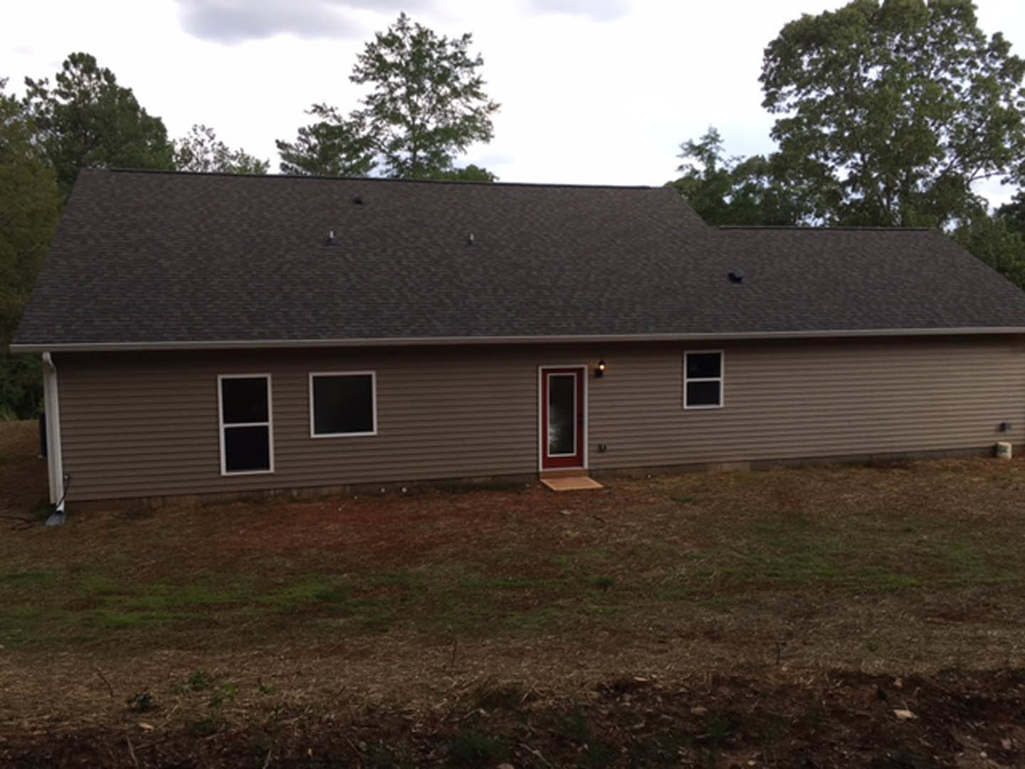 Two-story cottage with white siding, prominent red front door, white-framed windows, gabled roof, lush green lawn, leafy tree in foreground, partly cloudy sky overhead