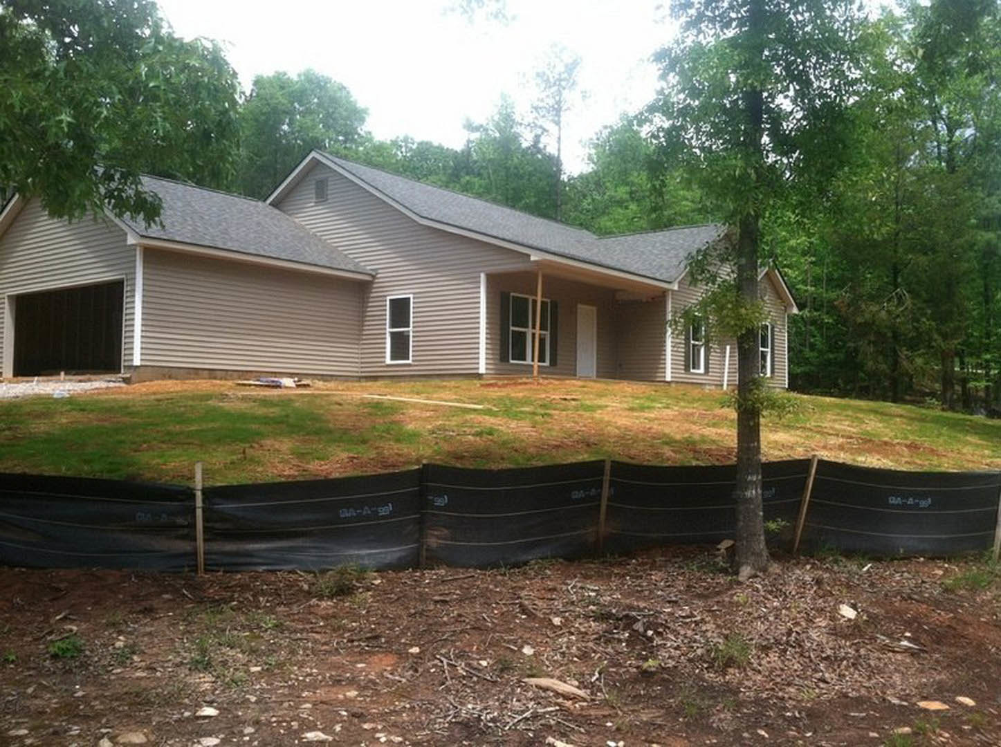 Two-story home with light siding, dark roof, and fenced yard; mature trees and grass surround the property.