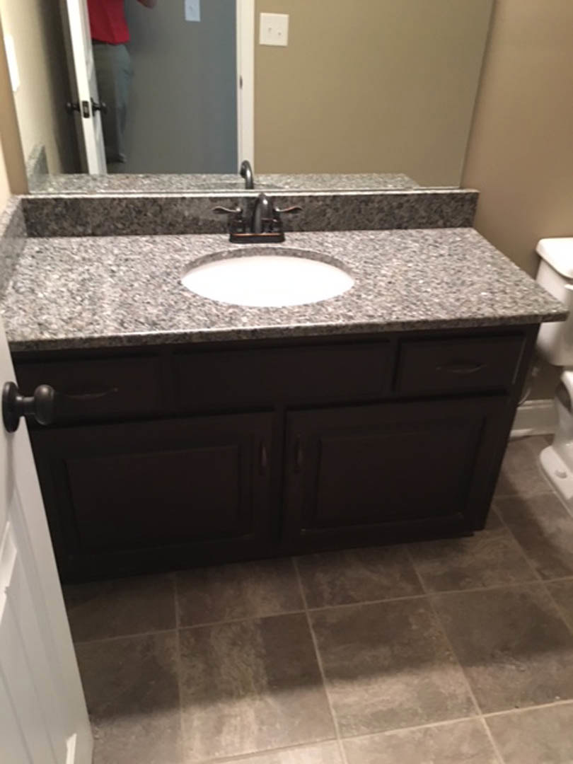 Marble countertop with undermount sink, chrome faucet, white cabinetry, wall-mounted mirror, and neutral painted walls in a bathroom.