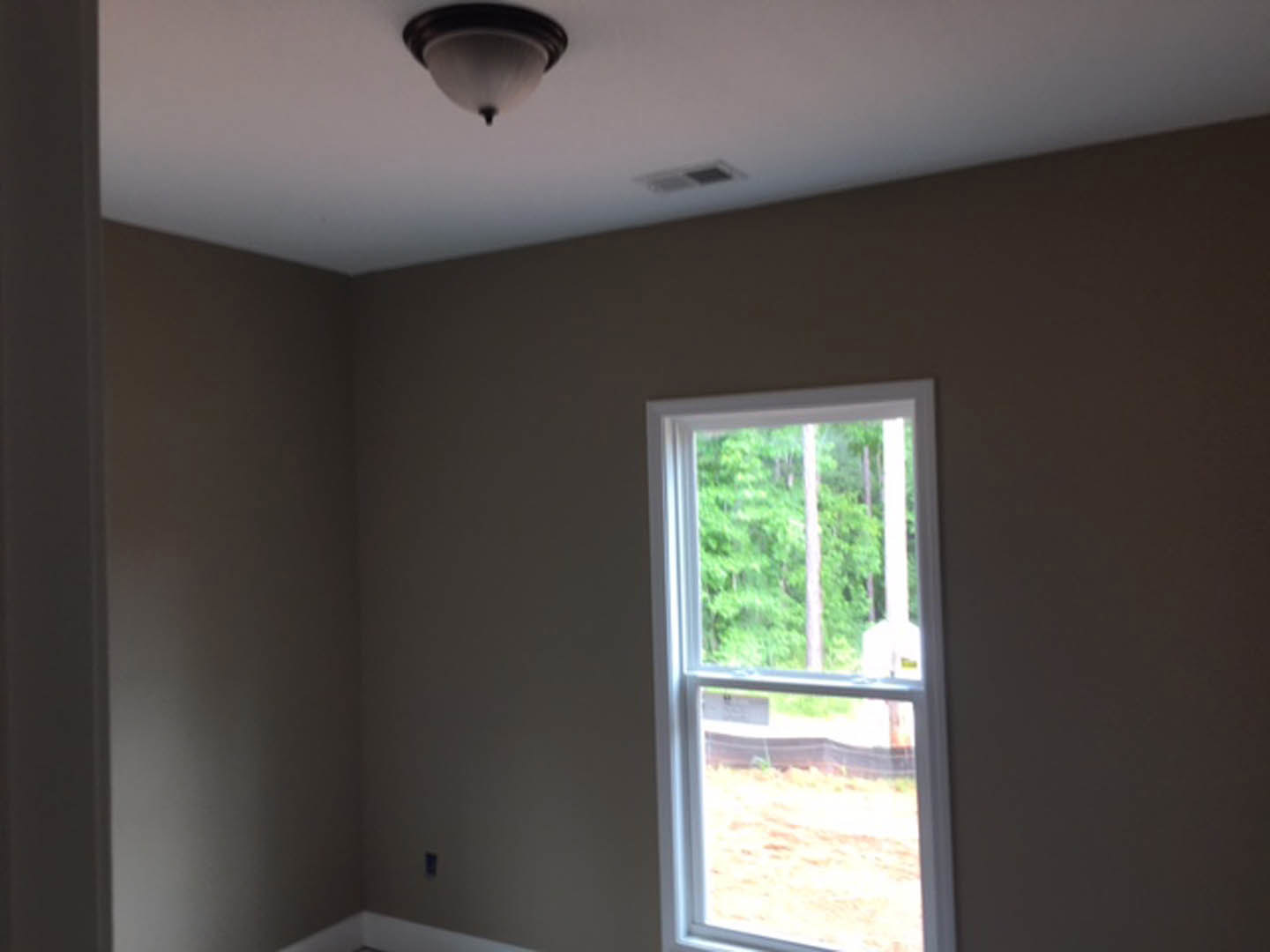 Bright room with white plaster walls, large window with blinds, ceiling fan and light fixture, natural daylight illuminating hardwood floor.