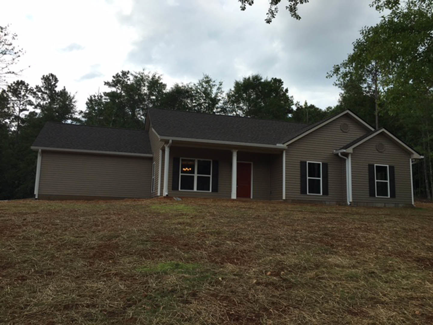 Two-story house with white siding, red front door, and white-framed windows set on a grassy hill under a cloudy sky