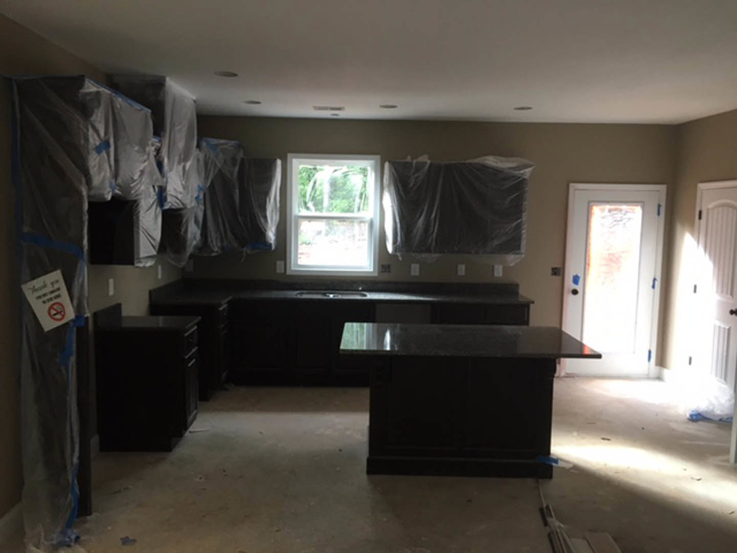 Kitchen featuring matte black cabinets and matching black countertops, stainless steel sink, white-framed window, light-colored flooring, and blue painter’s tape on the counter
