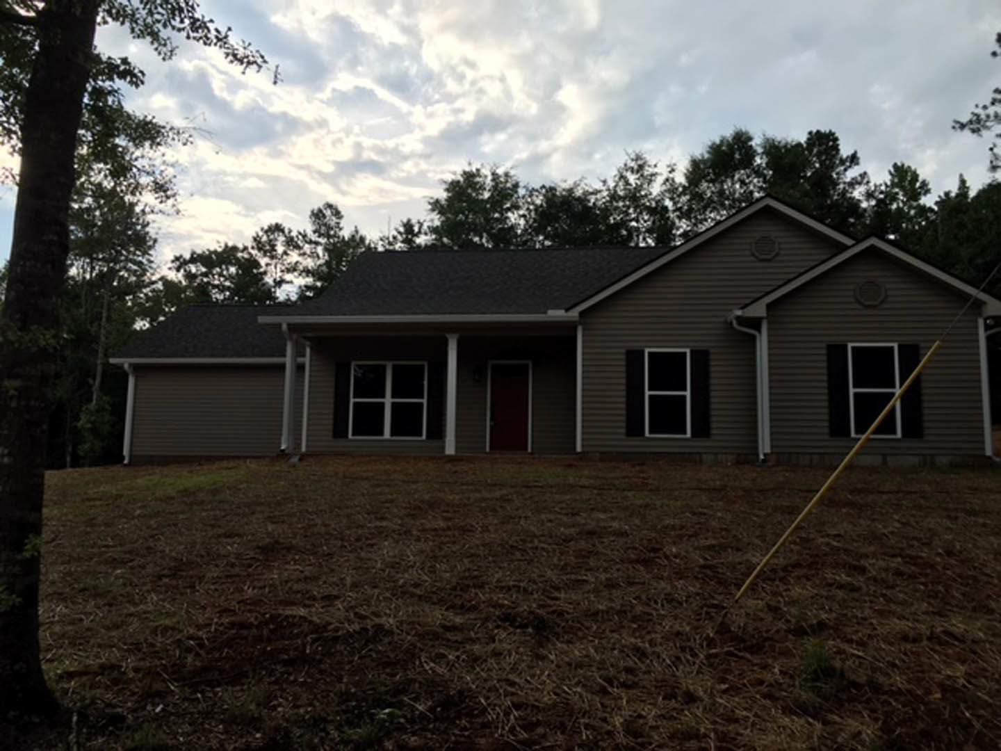 Two-story house with white siding, red front door, and multiple windows, surrounded by green lawn and mature trees under a partly cloudy sky
