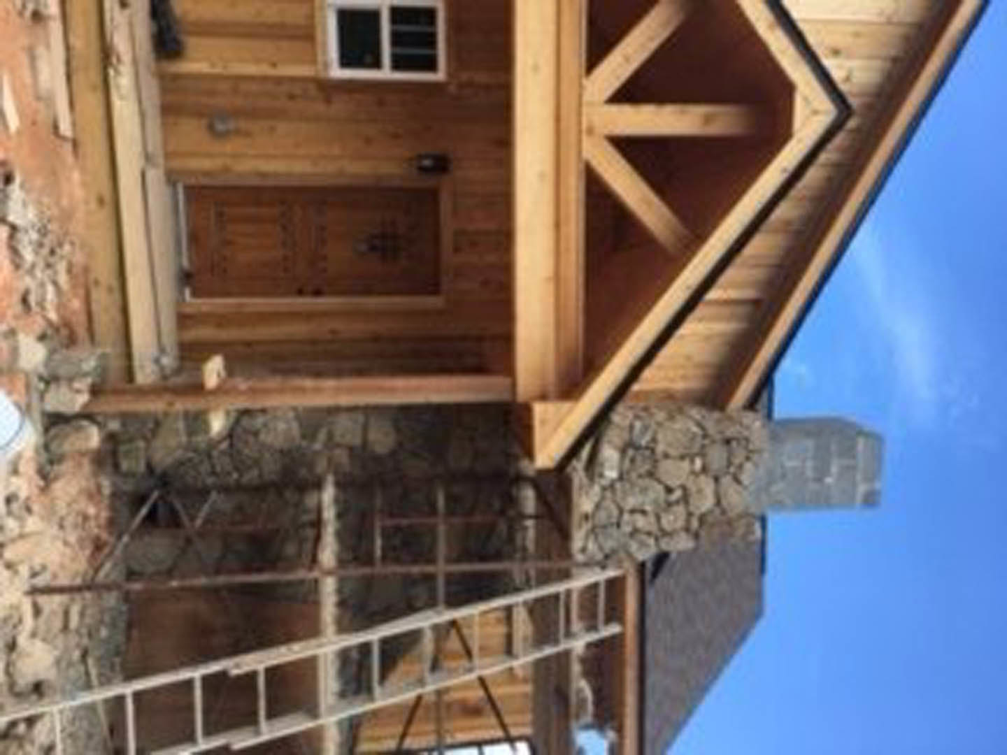 Wooden house exterior with plank siding, large window, and metal ladder leaning against the wall under a clear sky