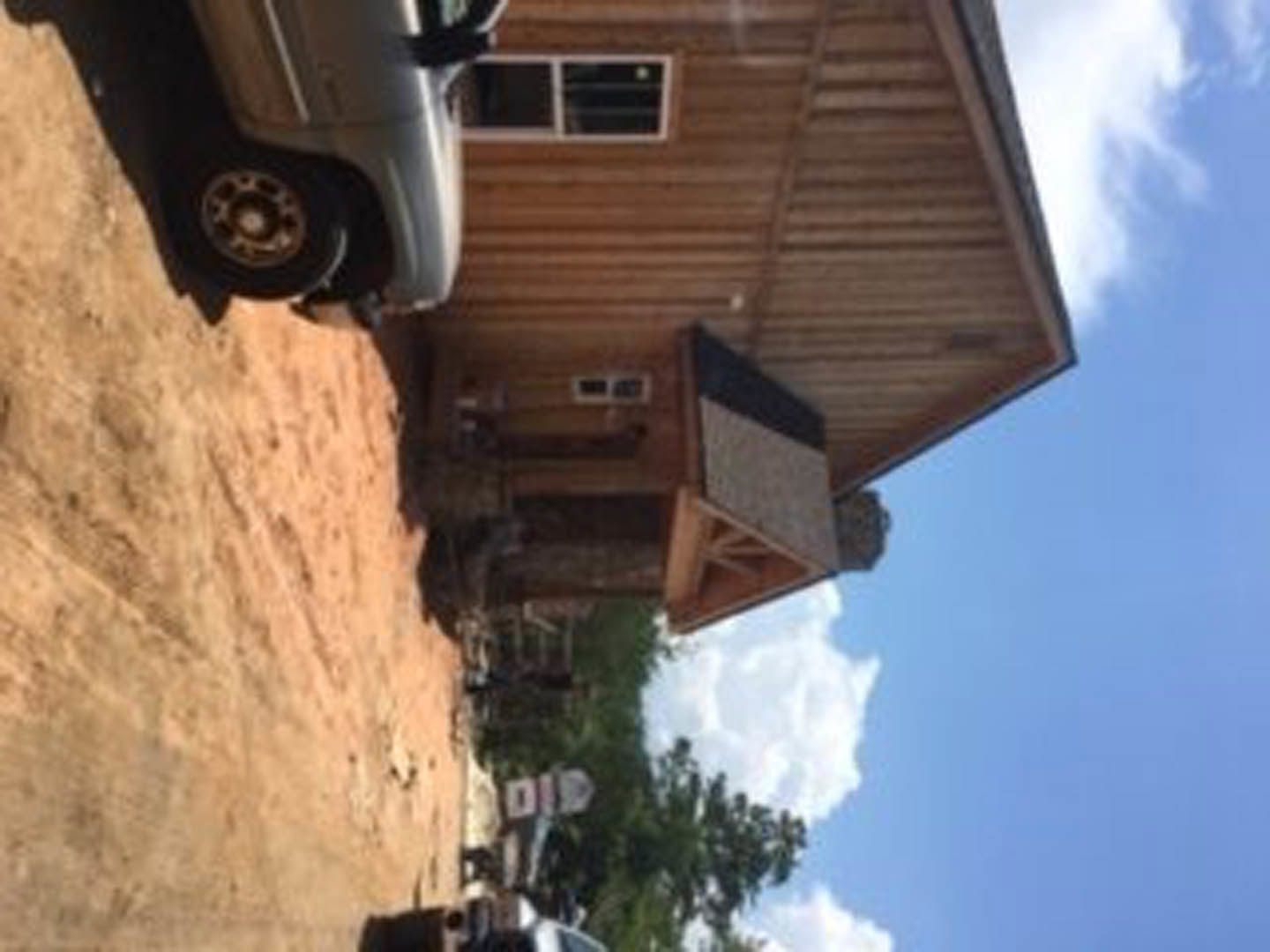 White sedan parked on concrete driveway in front of modern two-story house with gray siding, large windows, and manicured lawn under partly cloudy sky