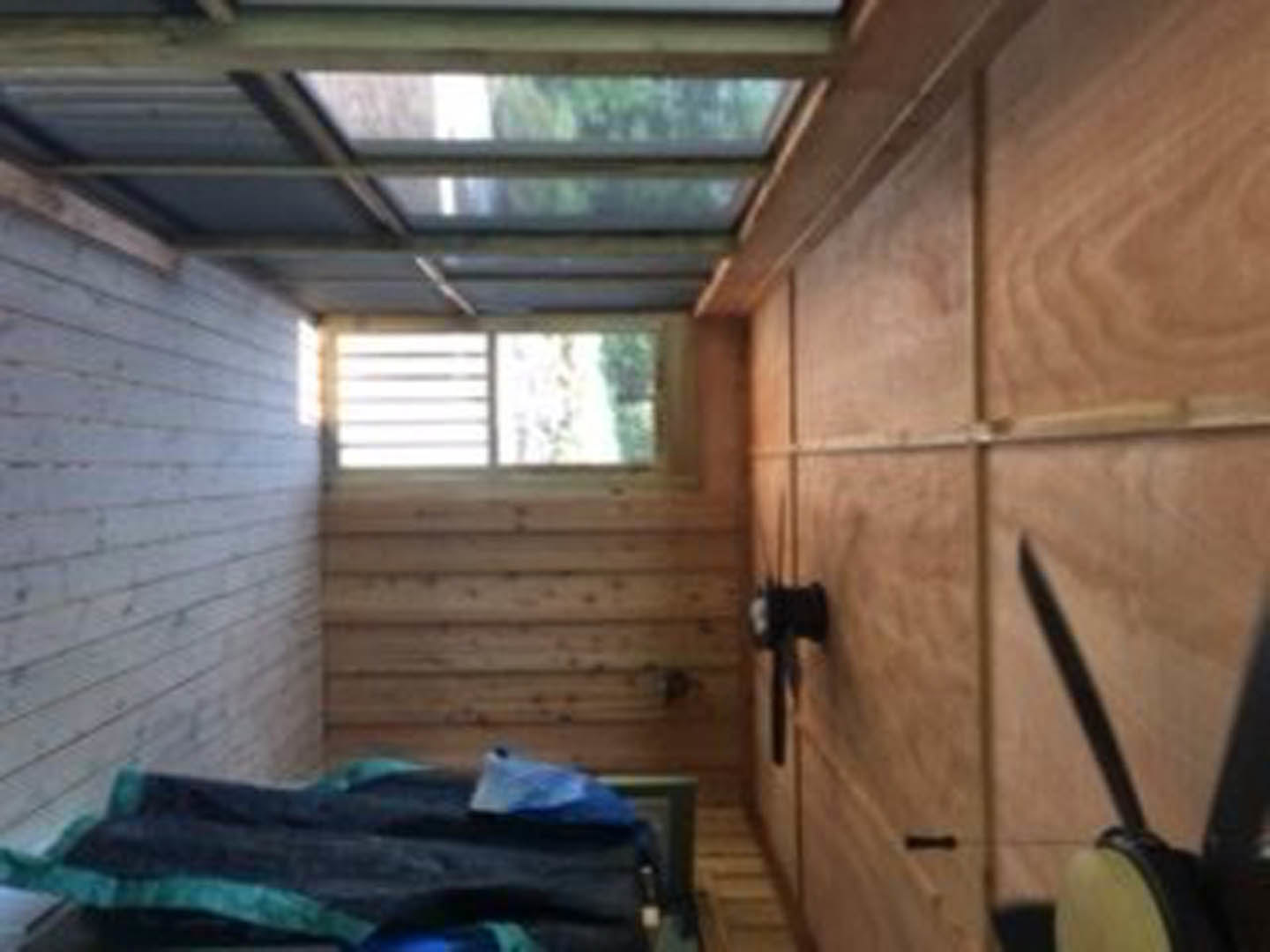 Sunlit room featuring hardwood floors, a large window with white trim, wooden door, exposed ceiling beams, and light-colored walls