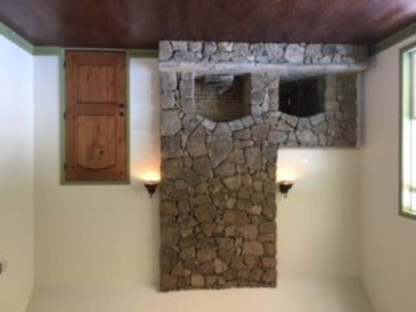 Stone fireplace with textured stone wall, two windows, and warm wood flooring in a spacious living room